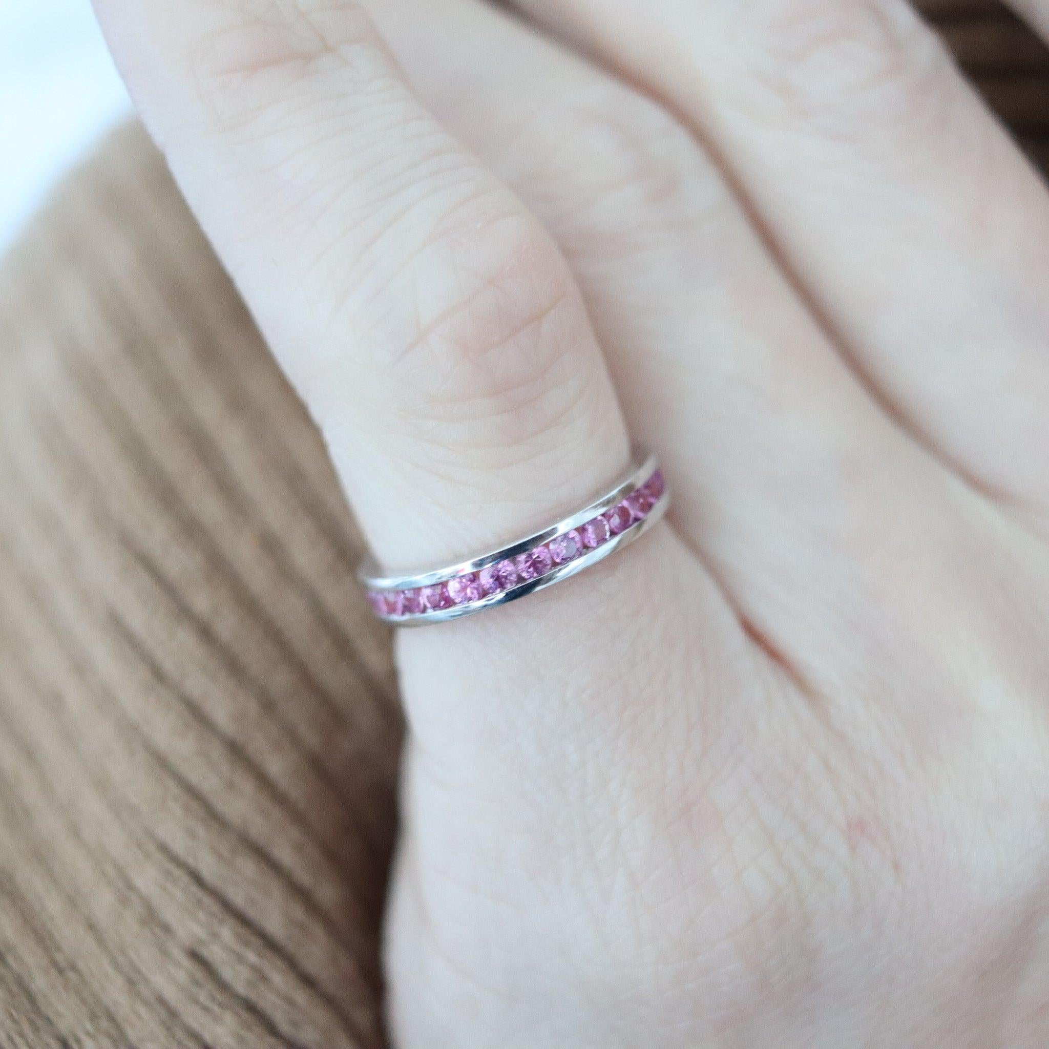 Un anello dell'eternità con zaffiri rosa.

Si tratta di una classica e moderna fascia a eternità piena realizzata con cura in oro bianco massiccio a 18 carati con finitura lucida. L'anello ha un design semplice ai lati ed è impreziosito da ventisei