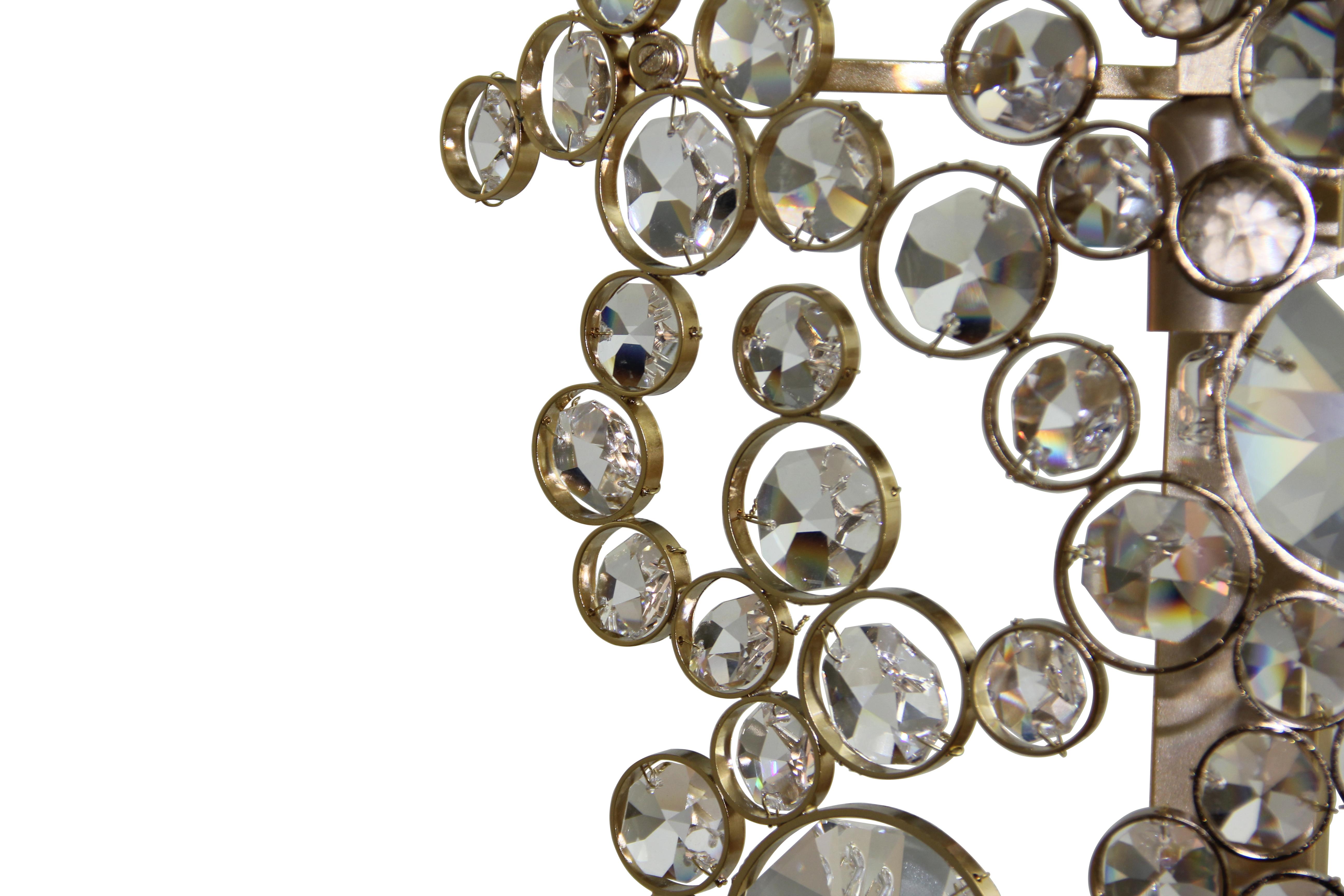 L'elegante silhouette di questa applique trae la sua brillantezza dalla sapiente applicazione del vetro. I cerchi eterni sono avvolti singolarmente in un metallo scintillante e posizionati con una sorprendente attenzione ai dettagli. Il risultato