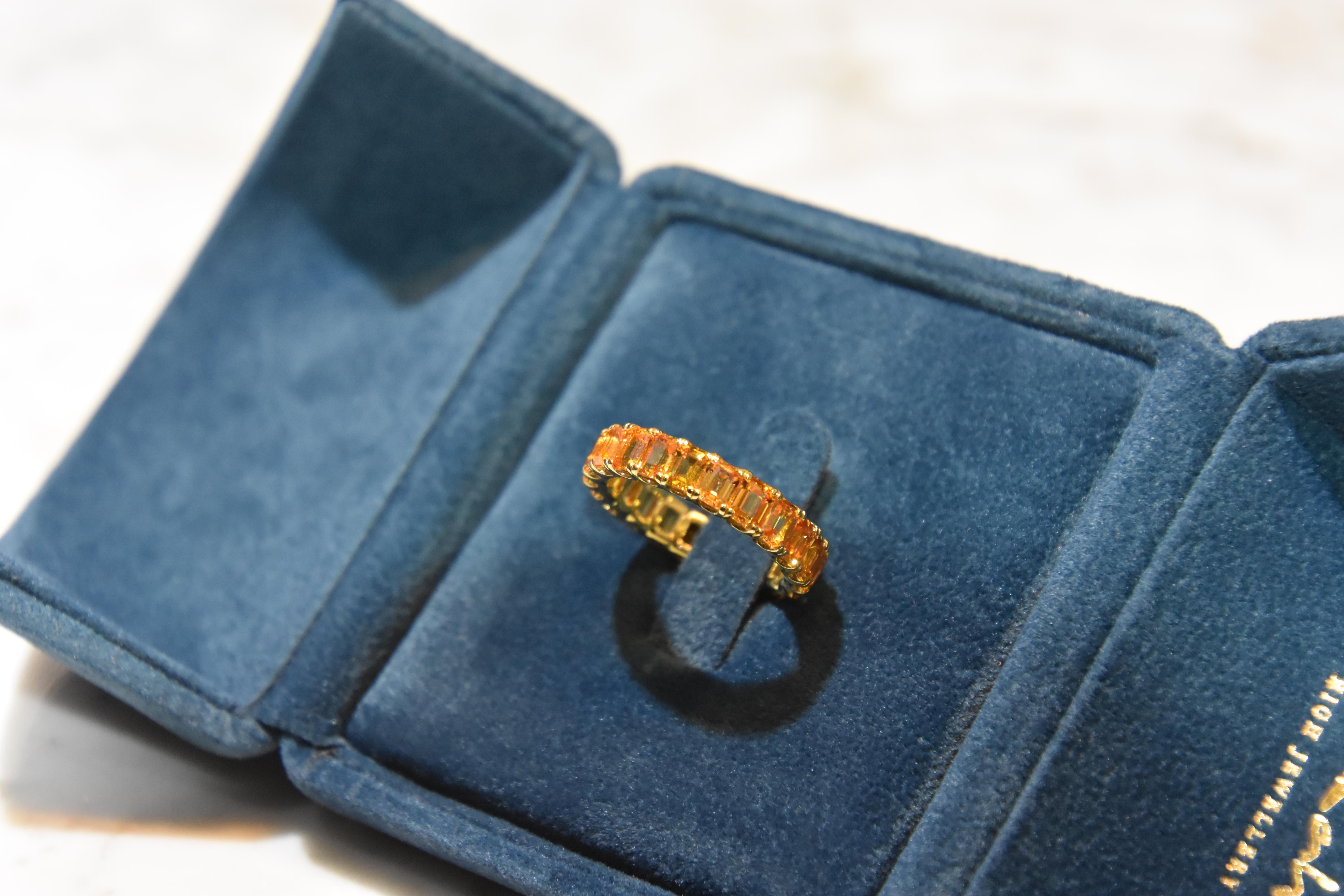 Uniform Orange sapphire Color with each stone 0.25 carat. Total 22pcs/ 5.65 carat Orange Sapphire Eternity Ring set in 18K yellow gold. You can order your own size. It takes around 4 weeks for delivery. 
Ring size- US 6.5 ,   Kahn also provide