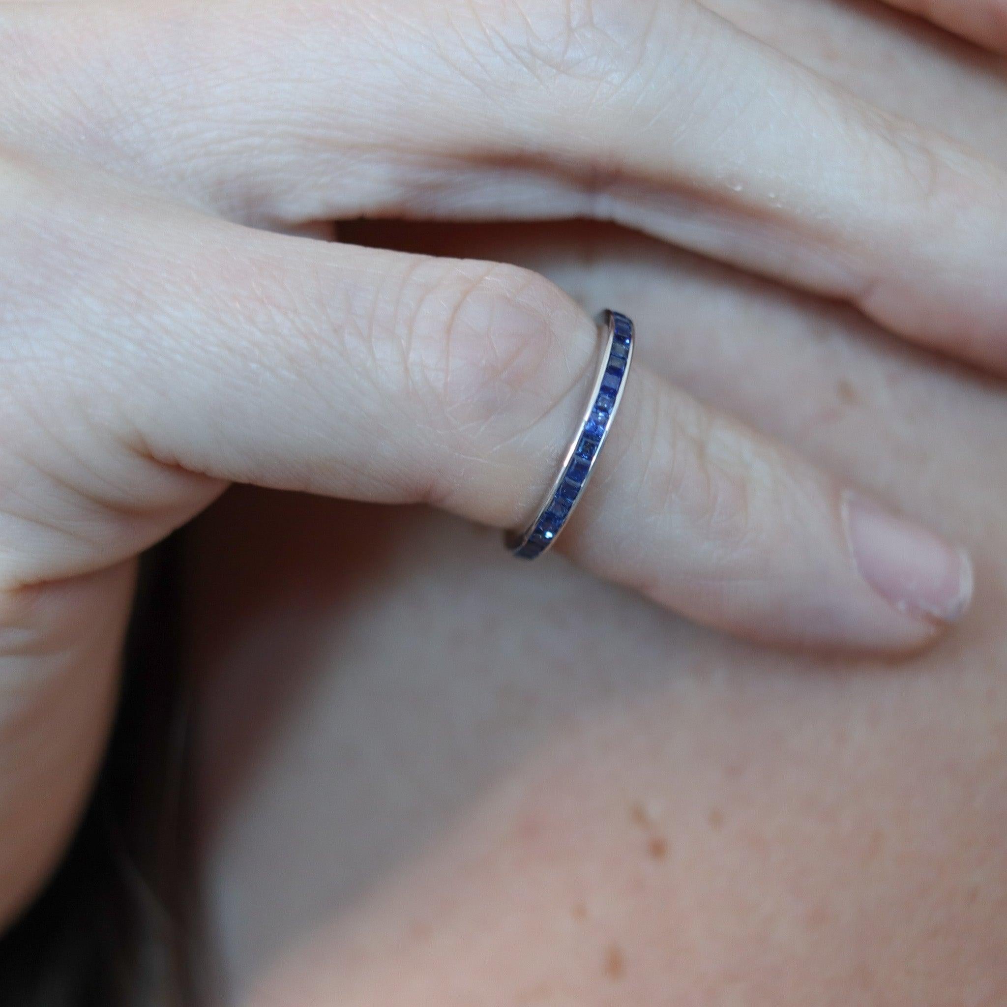 An eternity ring with sapphires.

This is a beautiful eternity band-ring, crafted with classic art deco patterns in solid white gold of 18 karats with high polished finish. The delicate ring feature a concealed channel, which is embellished with a