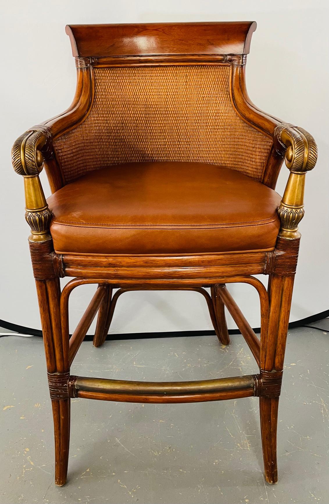 An elegant pair of Ethan Allen townhouse faux bamboo rattan bar stools featuring genuine leather seats and Fine wood carving details with cast metal in brass finish arms ending in scroll design. The stools are sturdy and their timeless style would