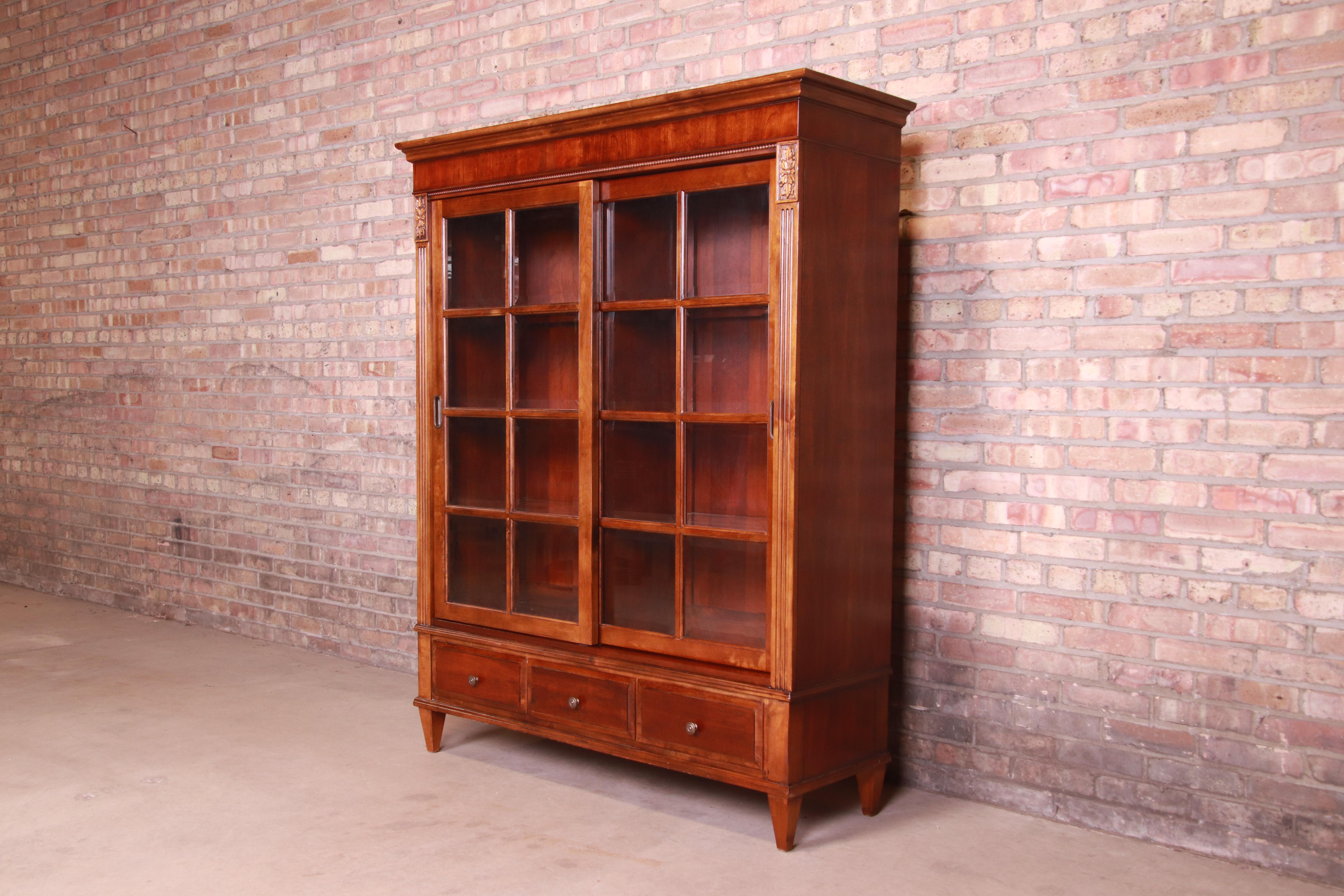 A gorgeous French Provincial or Regency style lighted display cabinet or bookcase

By Ethan Allen

USA, Circa 1990s

Carved cherry wood, with beveled glass front sliding doors.

Measures: 52.5