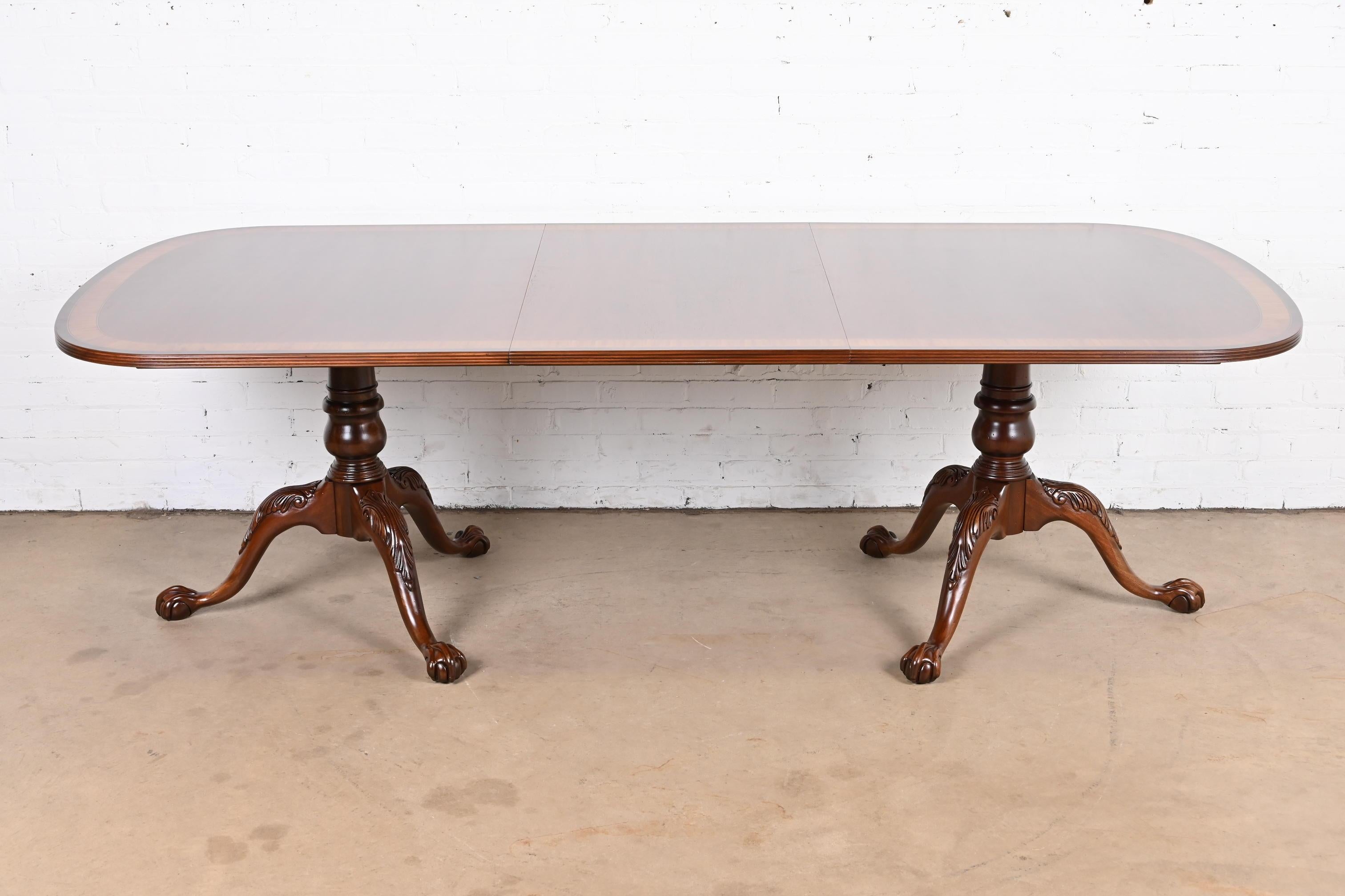 An exceptional Georgian or Chippendale style double pedestal extension dining table

USA, circa Late 20th century

Gorgeous book-matched mahogany, with satinwood banding, and carved solid mahogany pedestals with ball and claw feet.

Measures: 72