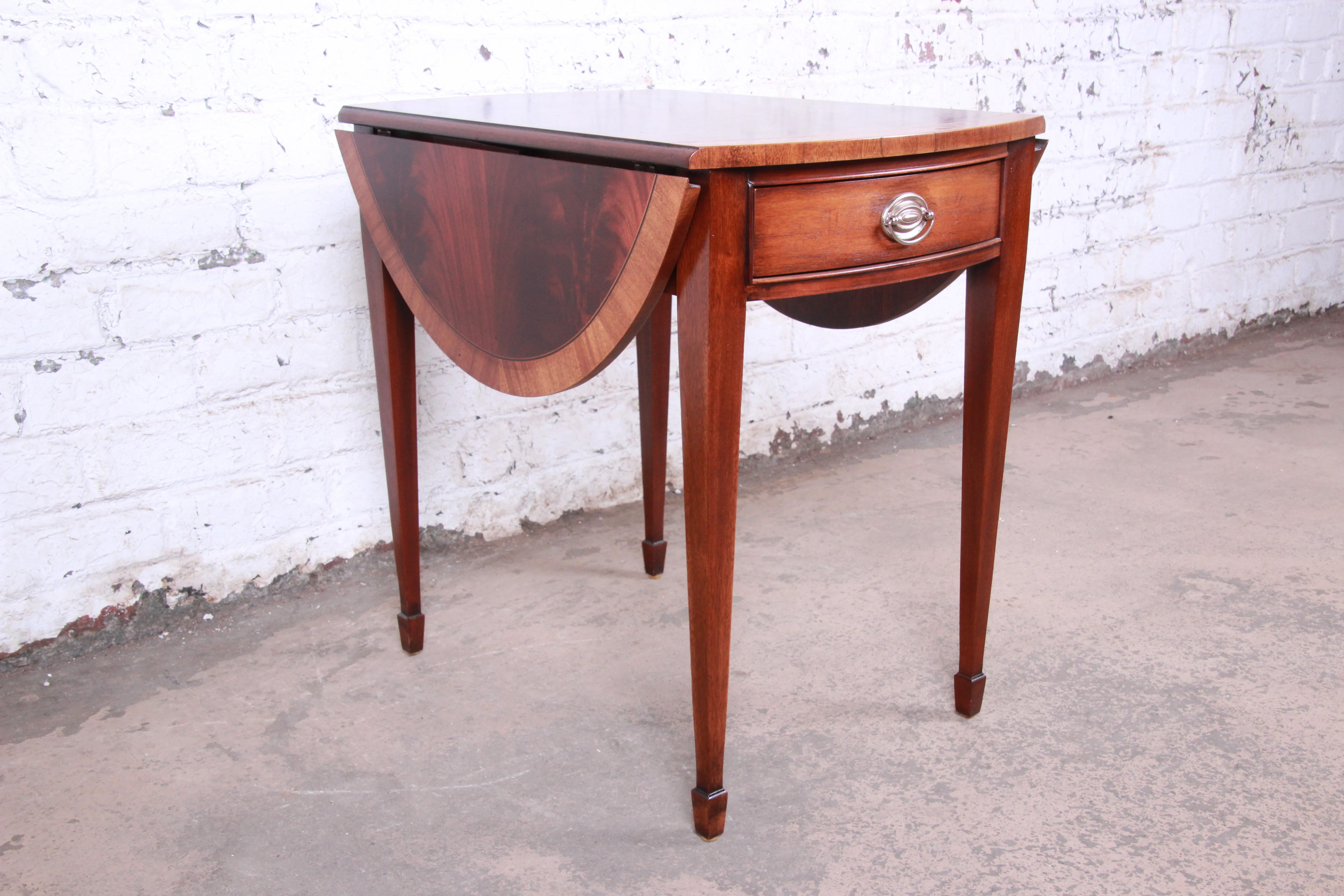 An exceptional Georgian style banded mahogany drop-leaf pembroke side table by Ethan Allen. The tables feature gorgeous flame mahogany wood grain with a banded edge. It offers good storage, with a single dovetailed drawer. The table has drop leaves