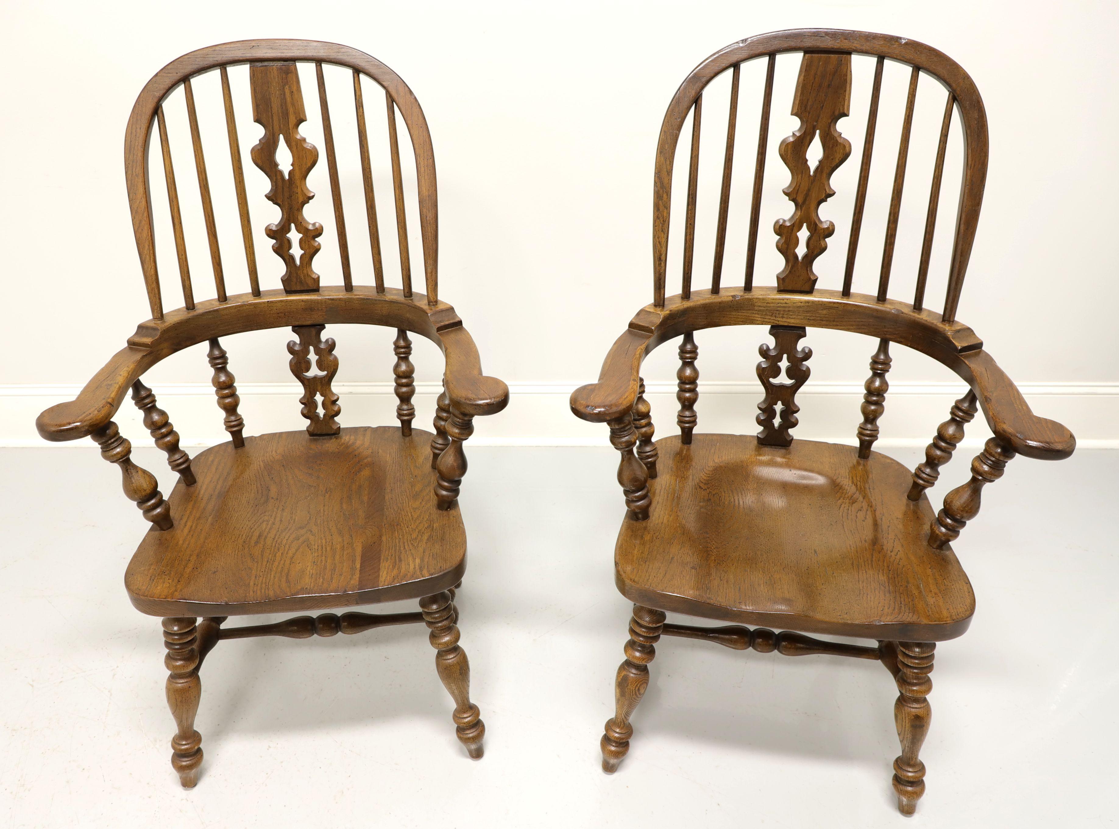 A pair of Windsor style dining armchairs by Ethan Allen, from their Royal Charter collection. Solid oak with bowback, spindle back with carved center backsplat, rounded arms, turned legs and stretchers. Made in the USA, in the late 20th Century.
