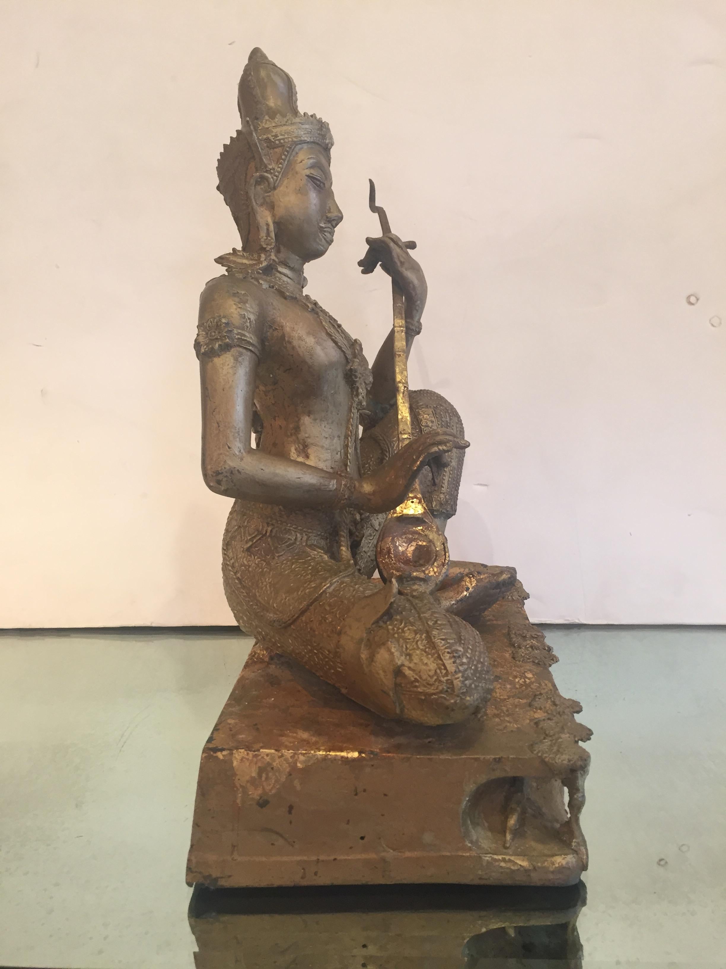 A lovely gilt bronze sculpture of a religious Thai deity sitting with one knee raised as he plays a musical instrument.