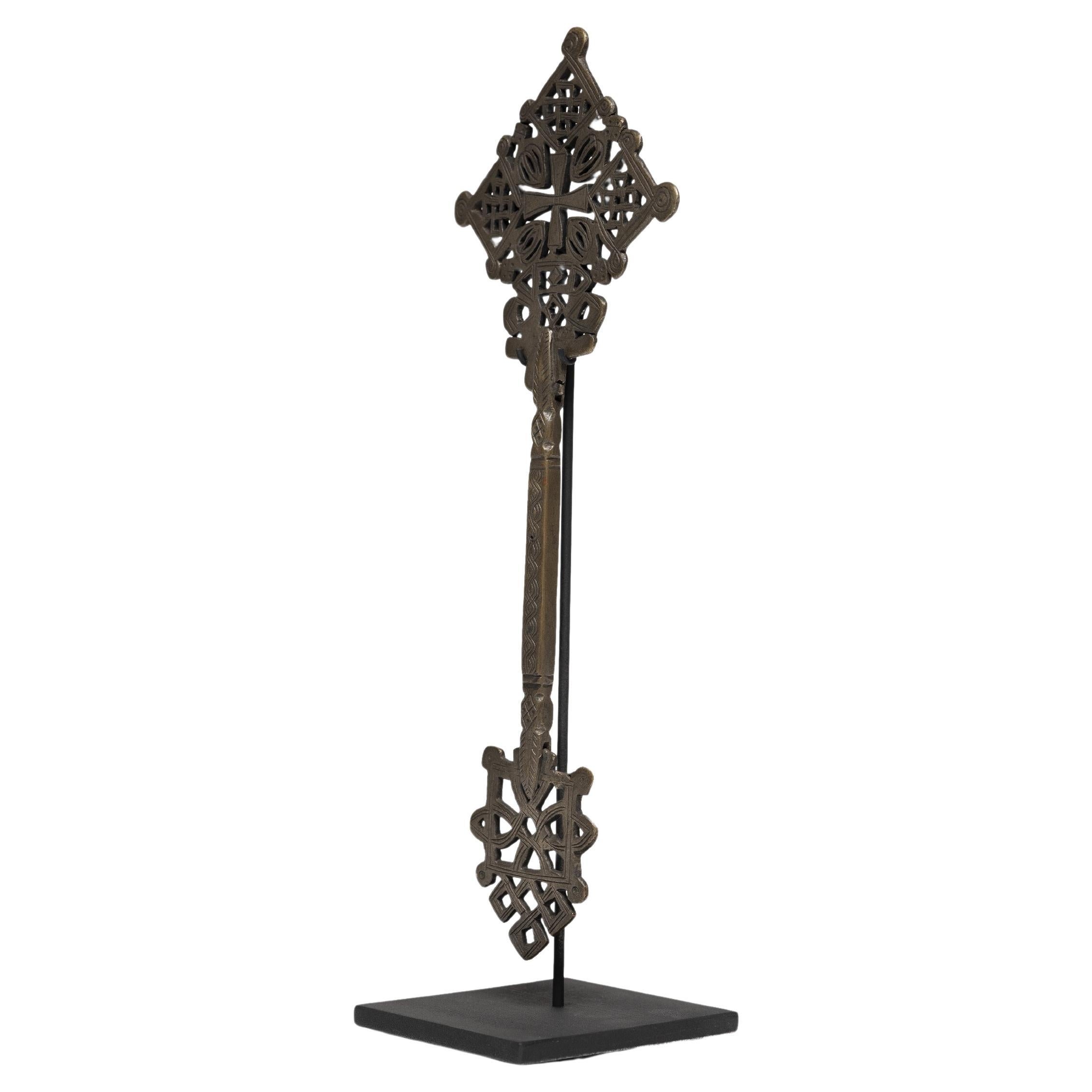 This intricate Ethiopian bronze cross exemplifies a style unique to the region's Coptic subset of the Christian faith. The exquisitely detailed perforated form is connected by a long etched handle, used primarily by priests. Integral to religious