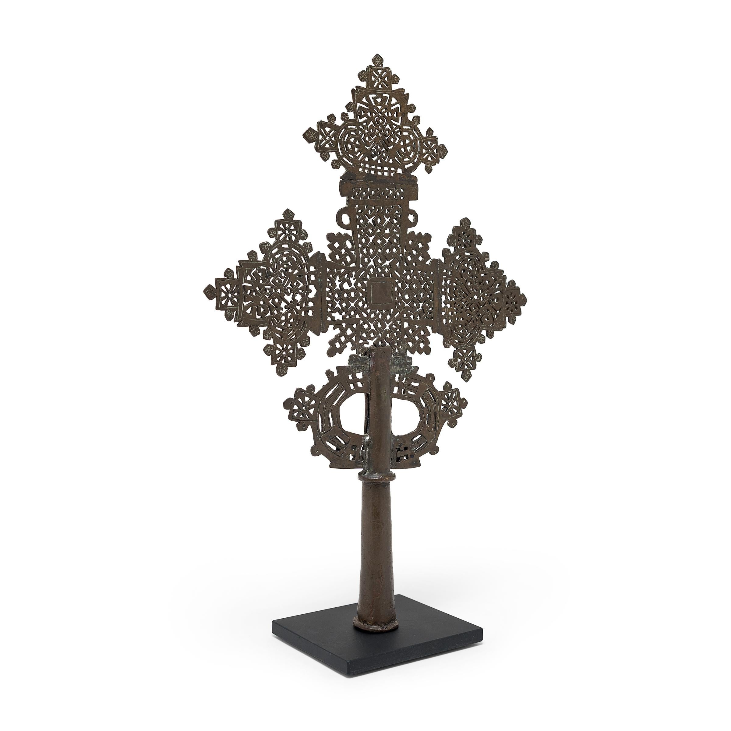 This intricate Ethiopian processional cross exemplifies a style unique to the region's Coptic subset of the Christian faith. The exquisitely detailed perforated form is centered on a hollowed base that could be either fitted upon a staff for