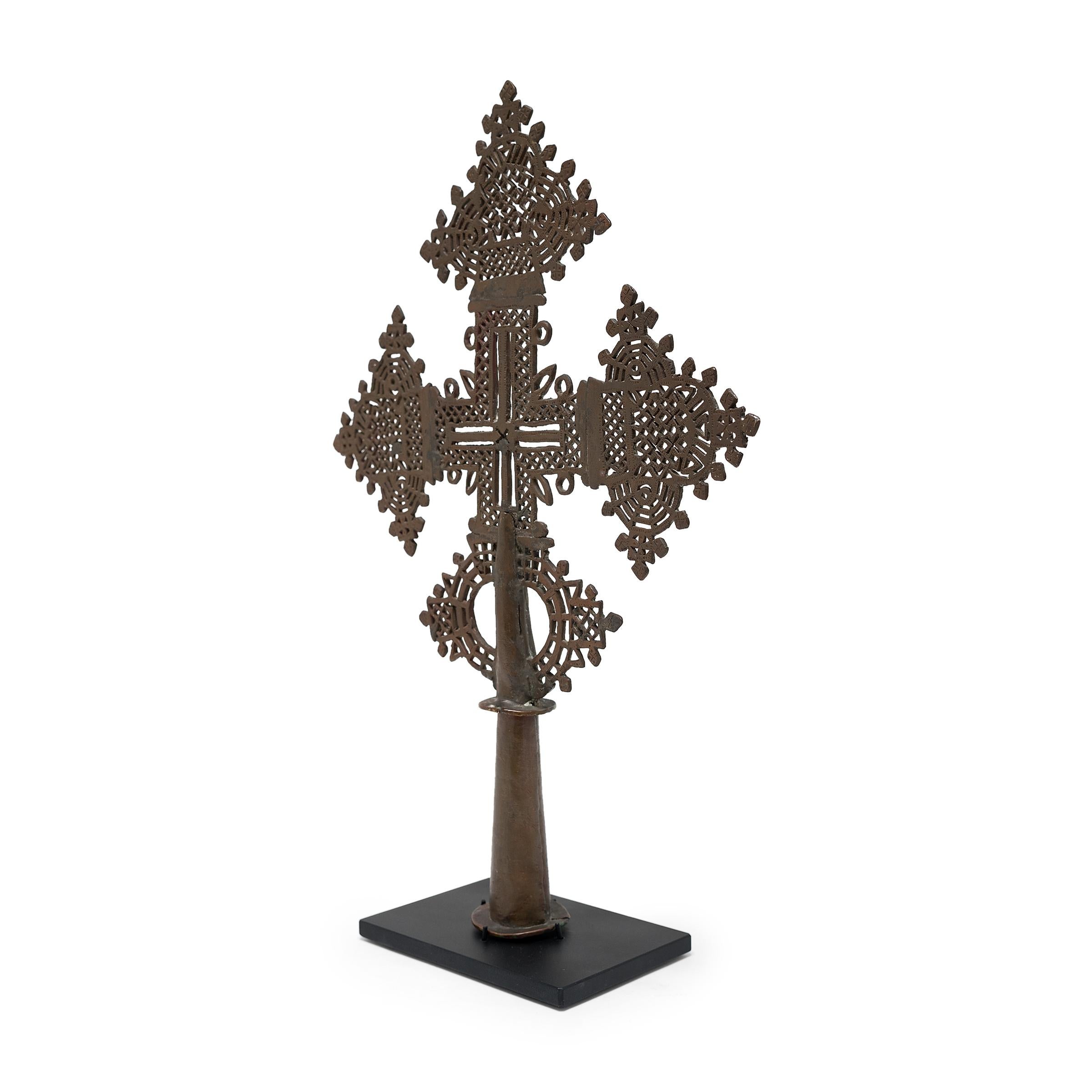 This intricate Ethiopian processional cross exemplifies a style unique to the region's Coptic subset of the Christian faith. The exquisitely detailed perforated form is centred on a hollowed base that could be either fitted upon a staff for