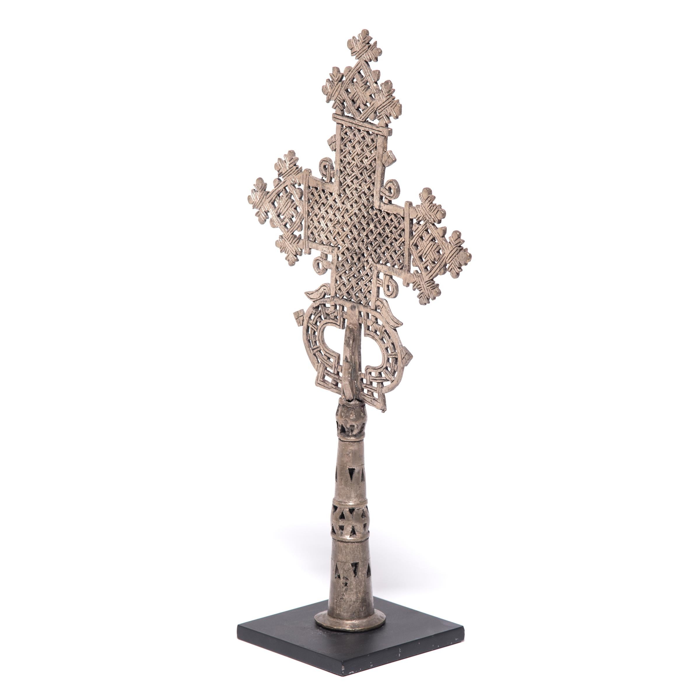 This intricate Ethiopian processional cross exemplifies a style unique to the region's Coptic subset of the Christian faith. The exquisitely detailed perforated form is centered on a hollowed base that could be either fitted upon a staff for