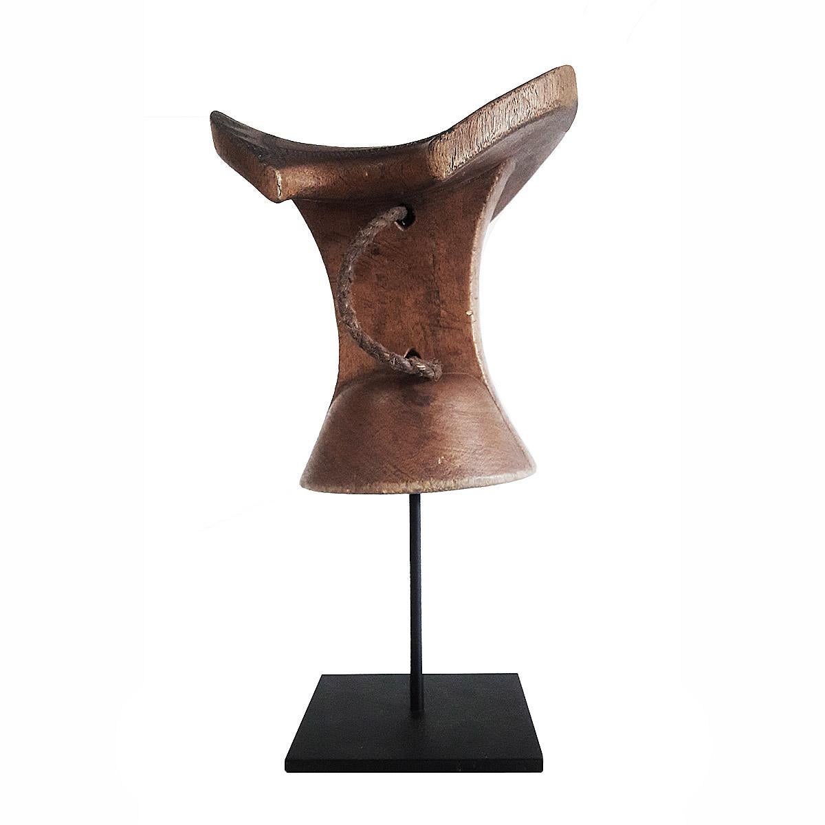 A headrest or stool, hand carved out of a single piece of teak wood, and decorated with traditional carvings, with a braided leather handle. Ethiopia, late 20th century. Mounted on a black metal stand.
