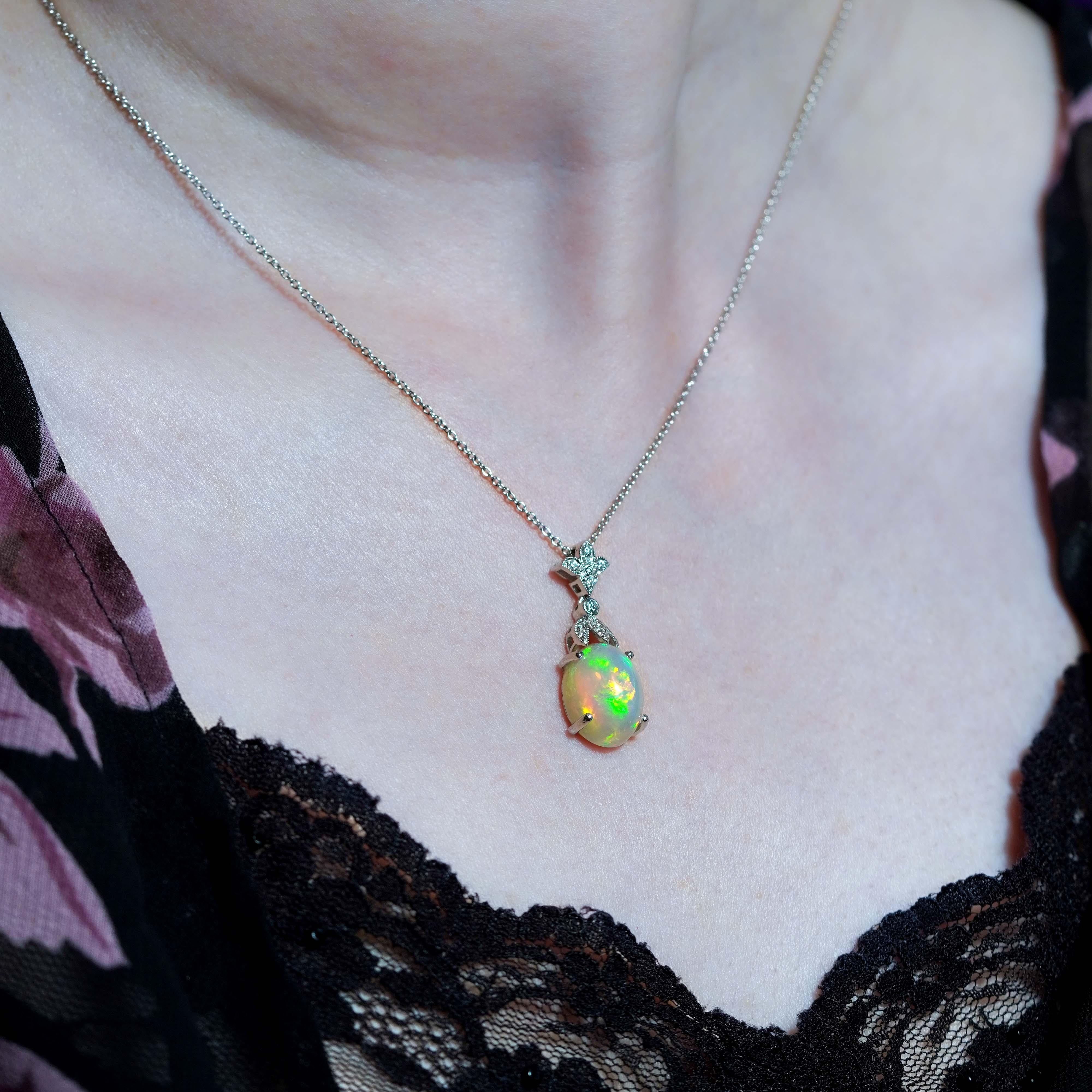 Features a luminous Ethiopian opal—renowned for its vibrant play of color and natural fire. The opal shifts beautifully with every movement, revealing flashes of green, gold, pink, and blue. Hanging the opal, brilliant white diamonds are