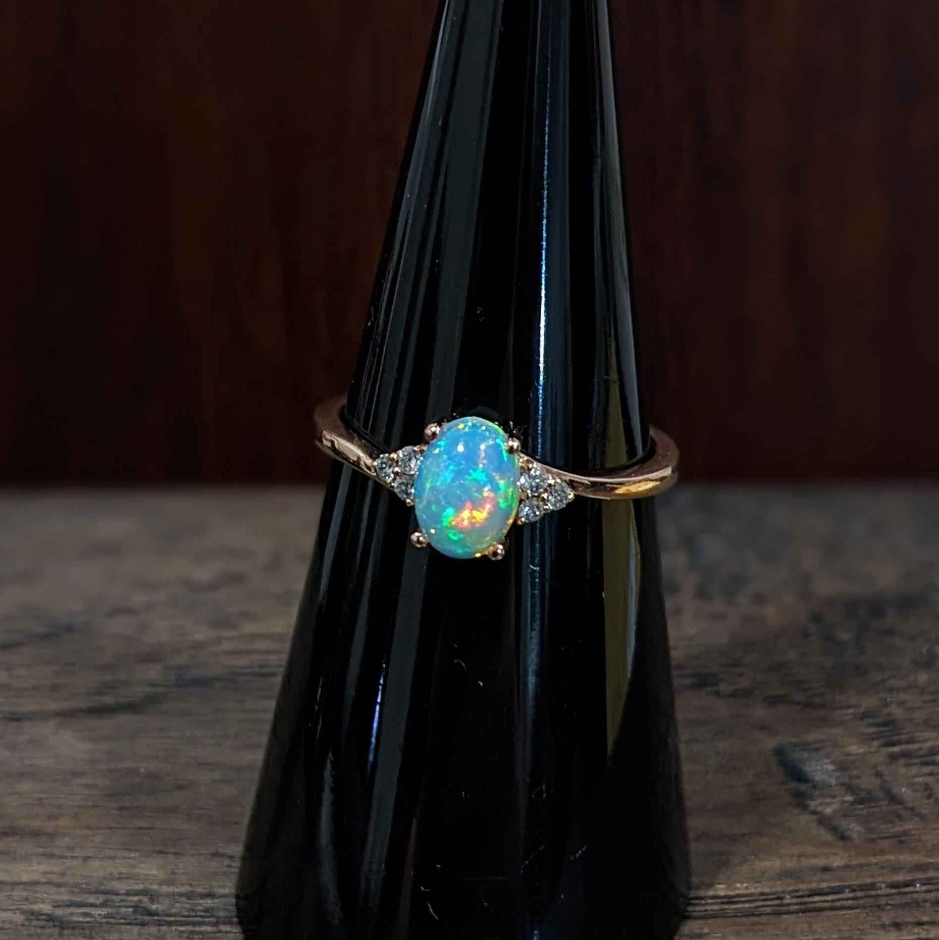 This lovely opal has all the colors of the rainbow, accented with natural earth mined diamonds set in 14k yellow gold. An elegant bypass ring design makes this glowing oval ring perfect for the modern bride or that special someone in your life! This
