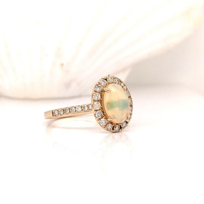 A beautiful 14k solid gold ring featuring a 7x5 mm colorful opal center stone with a beautiful halo of earth mined natural diamonds. This ring has a cathedral pave shank and prongs to hold the opal. This unique piece is perfect for any outfit or