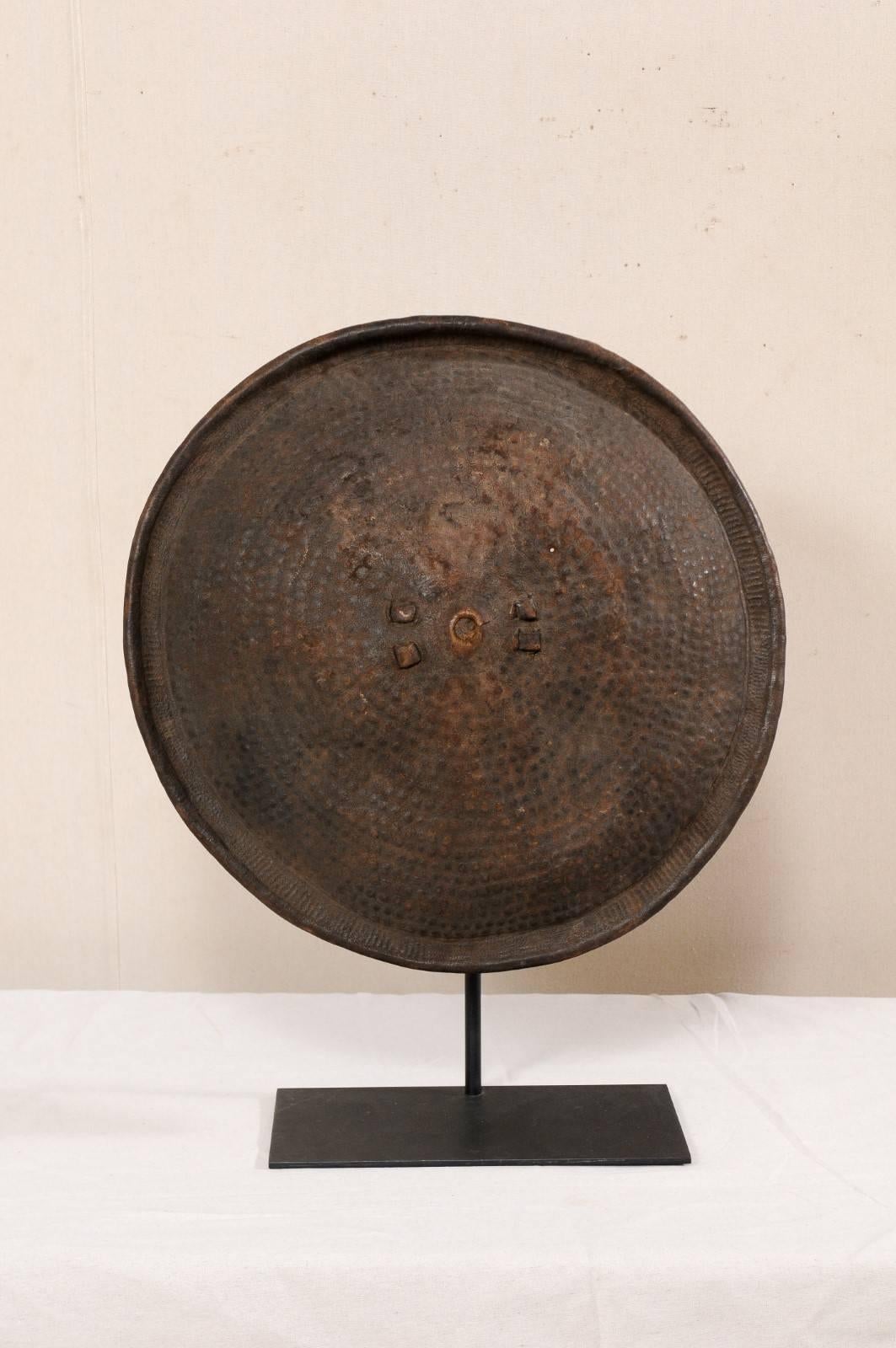 An Ethiopian tribal shield on custom iron stand. This vintage shield, originating from Ethiopia, has an overall convexly rounded-shape, and is made of a rich brown animal hide with wonderful patina. The leather shield is decorated with tooled