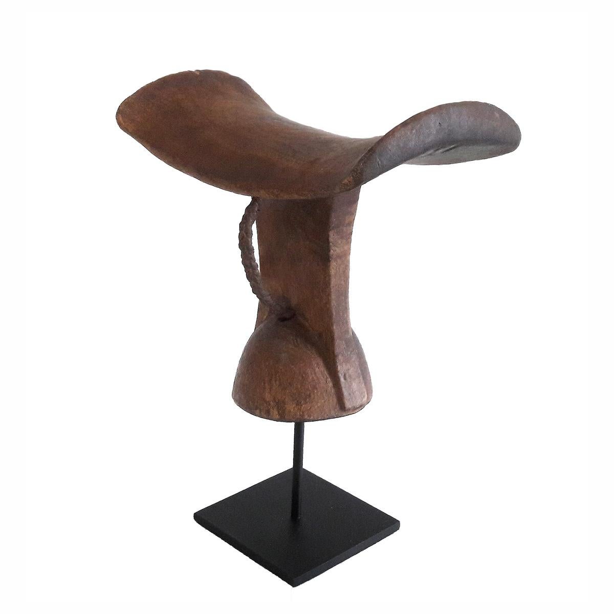 A headrest or stool, hand carved out of a single piece of teak wood. From Ethiopia, late 20th century. Mounted on a black metal stand.