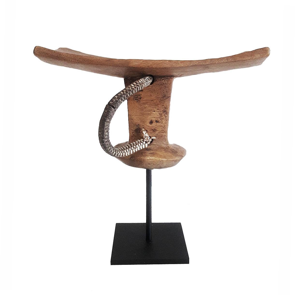 A headrest or stool, hand carved out of a single piece of teak wood. From Ethiopia, late 20th century. Mounted on a black metal stand.