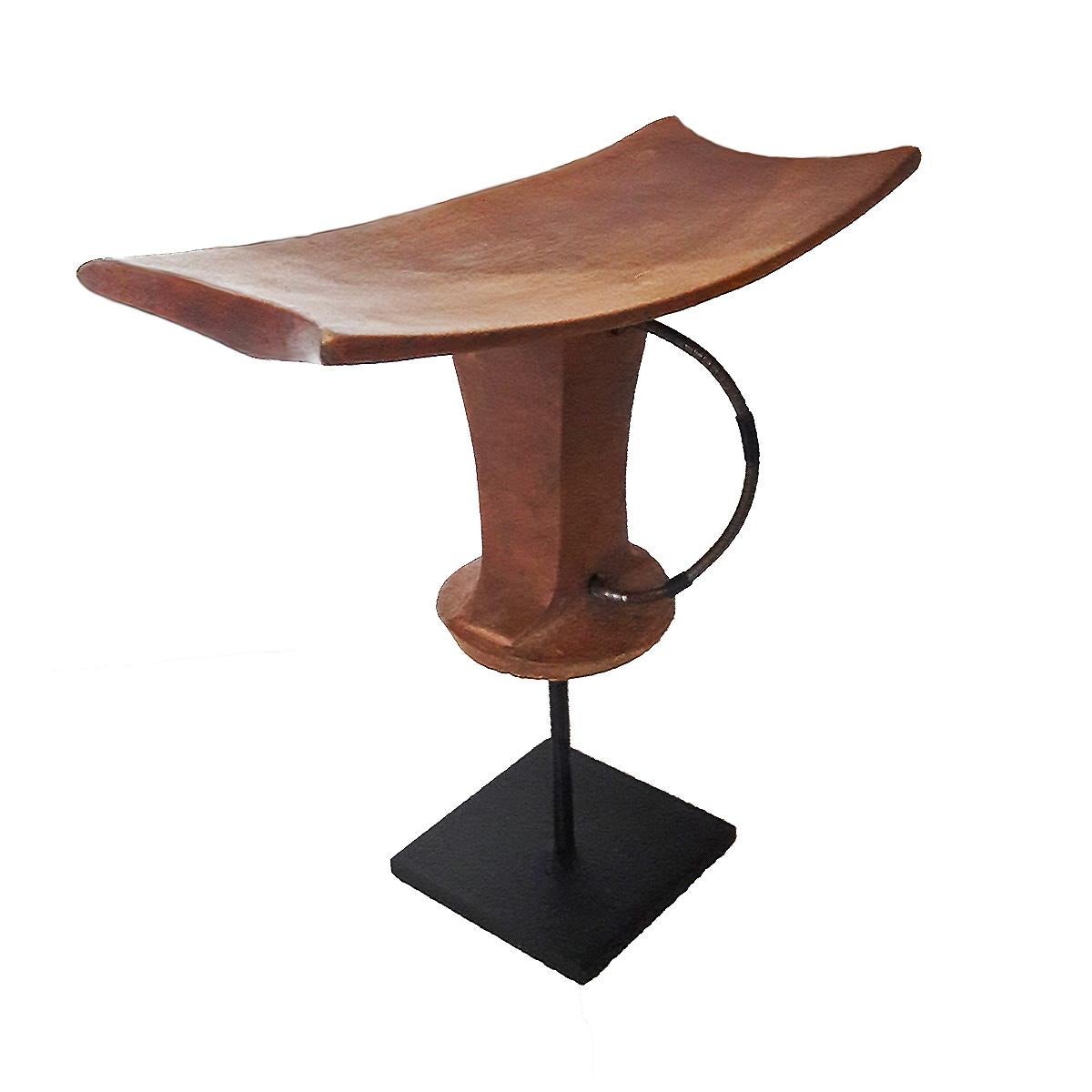 A headrest or stool, hand carved out of a single piece of teak wood and a metal carrying cord. From Ethiopia, late 20th century. Mounted on a black metal stand.