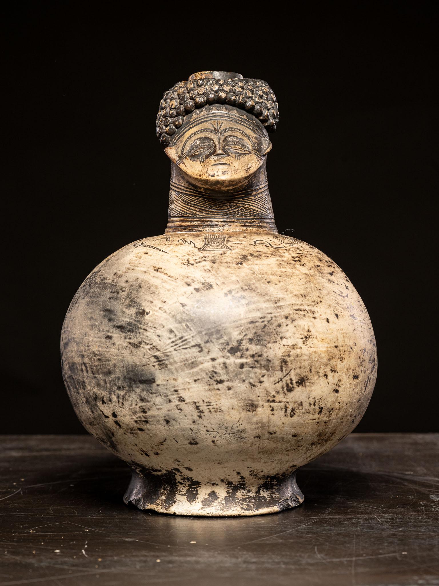This vessel is a striking example of anthropomorphic design, clearly incorporating human characteristics into its form. The upper section features a finely detailed human face, complete with stylized eyes, nose, lips, and an elaborate headdress or