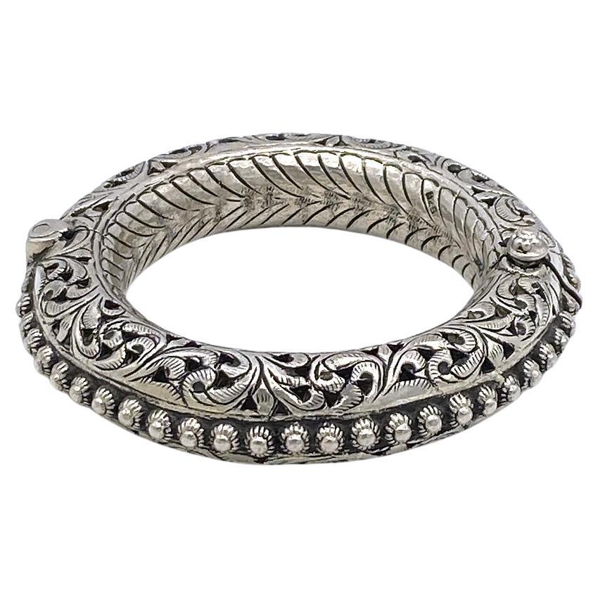 This is a bold ethnic sterling silver bangle. This dramatic 108g marked 925 handcrafted bangle with detailed pierced leaves pattern and traditional Indian style is hinged and has a pull-pin clasp. It has a 11.38 inch outer circumference with 7 inch