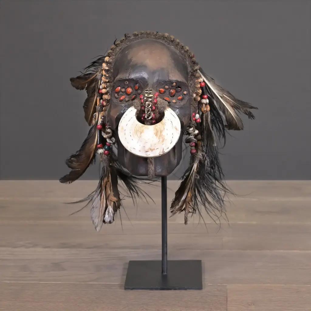 This handcrafted tribal trophy skull replica from Irian Jaya, Papua New Guinea, is a striking piece of ethnic decor that reflects the ancestral warrior traditions of the Papuan tribes. Made from sculpted resin and adorned with natural feathers,