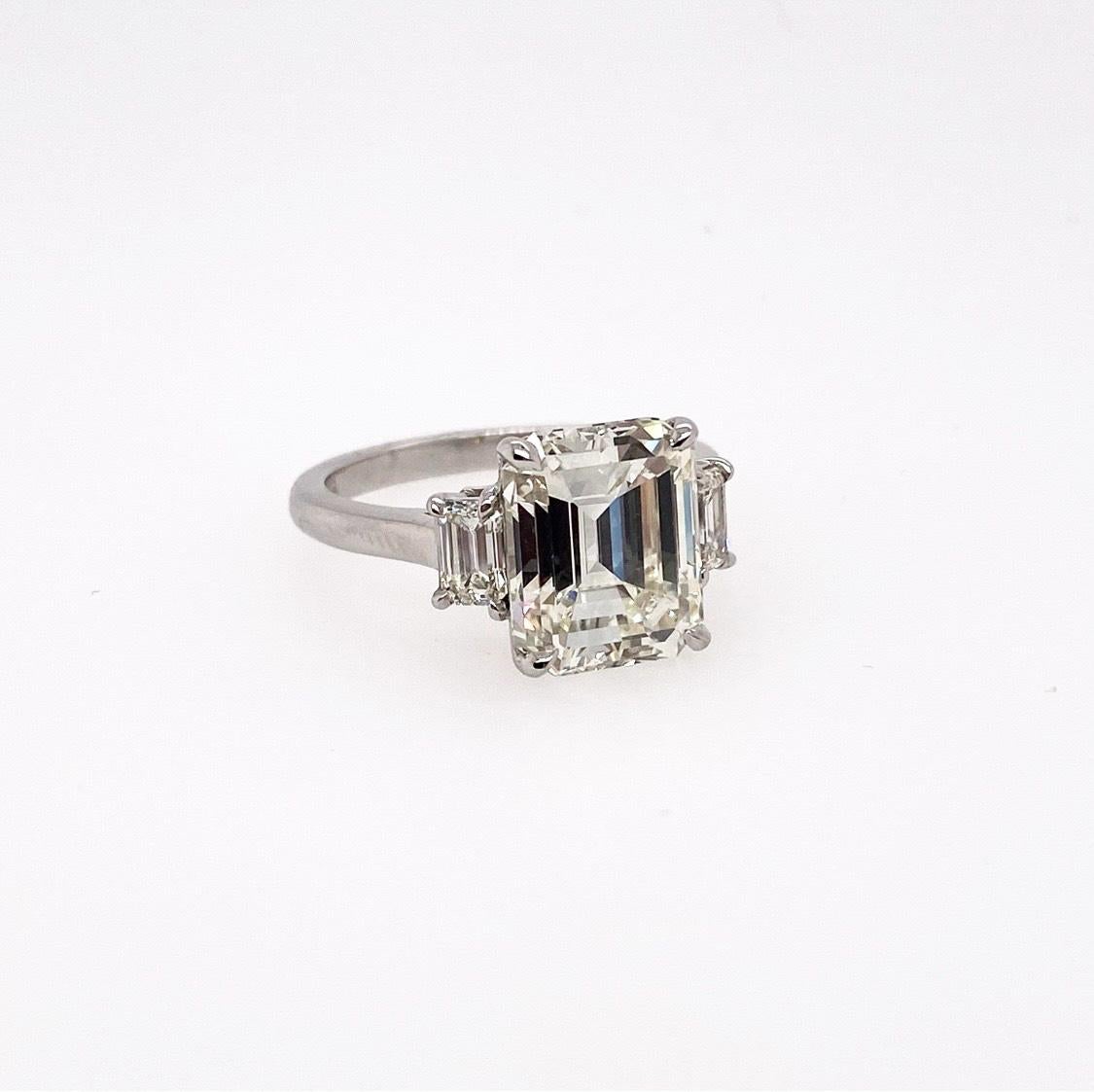 GIA Certified 4.69 carat Emerald Cut diamond is perfectly accentuated with another two beautifully emerald cut diamonds mounted on the side of the ring respectively. This stylish three-stone ring features the sophisticated statement and the