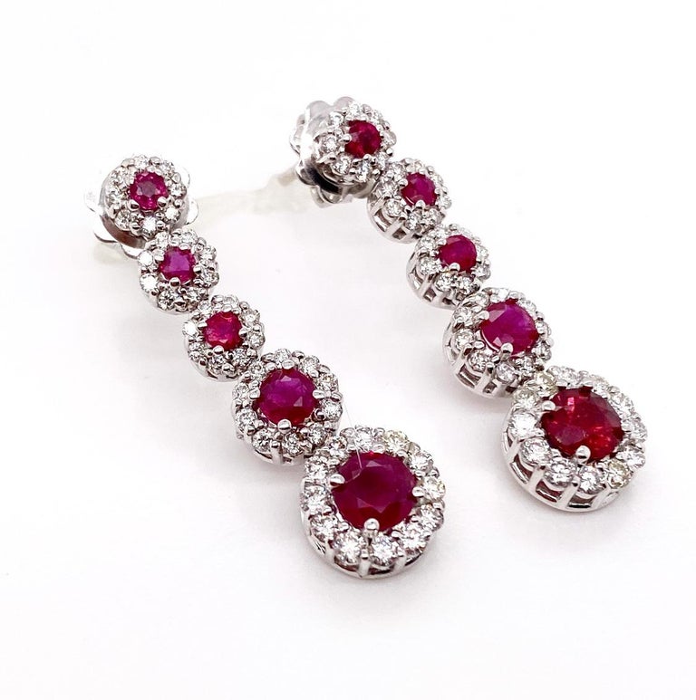This elegant earrings features a deep reddish, round faceted ruby surrounded by a halo of round brilliant-cut diamonds set in 18K white gold. Each earrings is consisting of five graduating ruby and diamond clusters so, this beautiful pair of