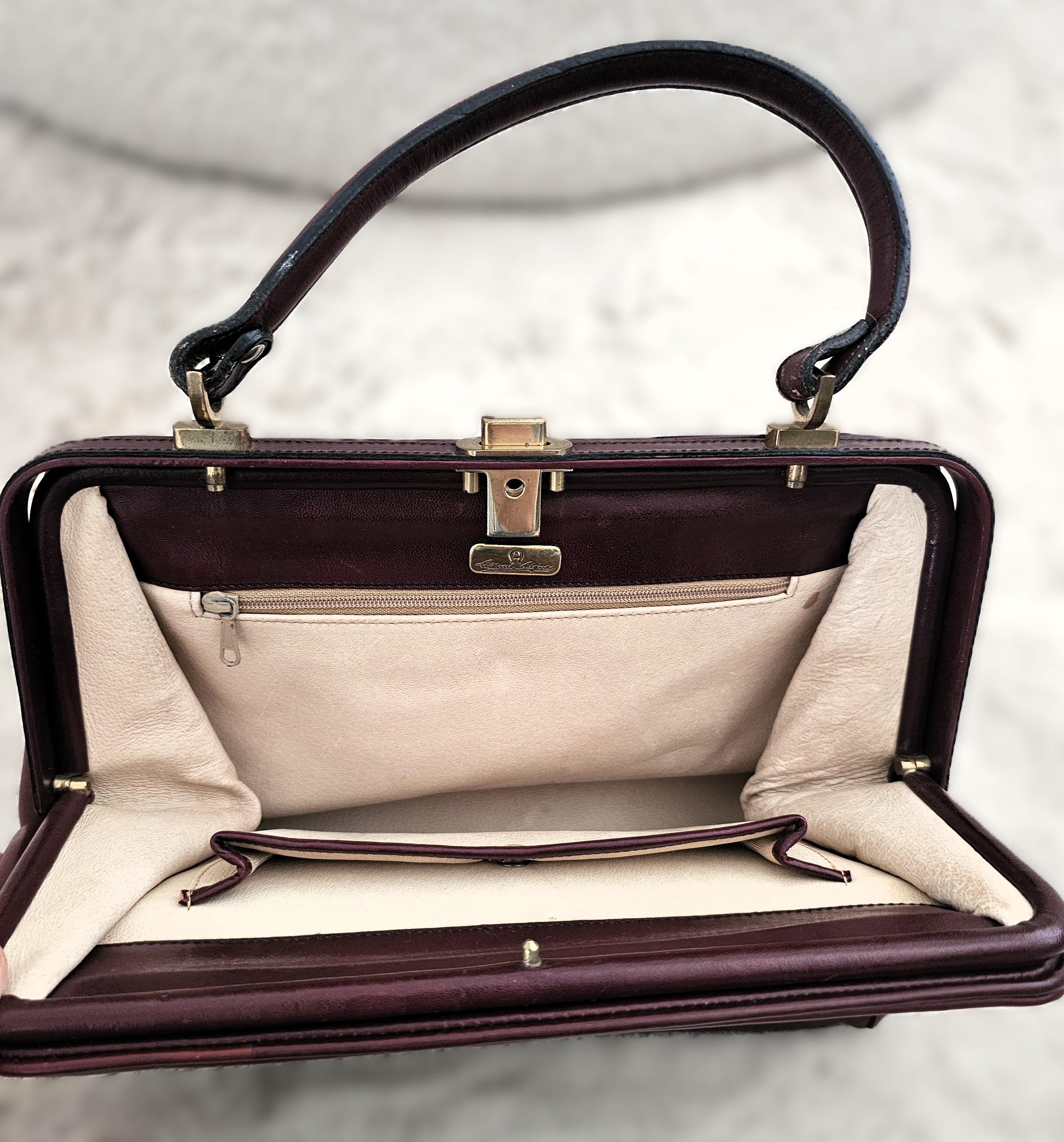 Diese außergewöhnliche Aigner-Tasche aus den 1980er Jahren ist ein seltenes Sammlerstück, gefertigt aus hochwertigem Glattleder in einem satten Rotbraun (