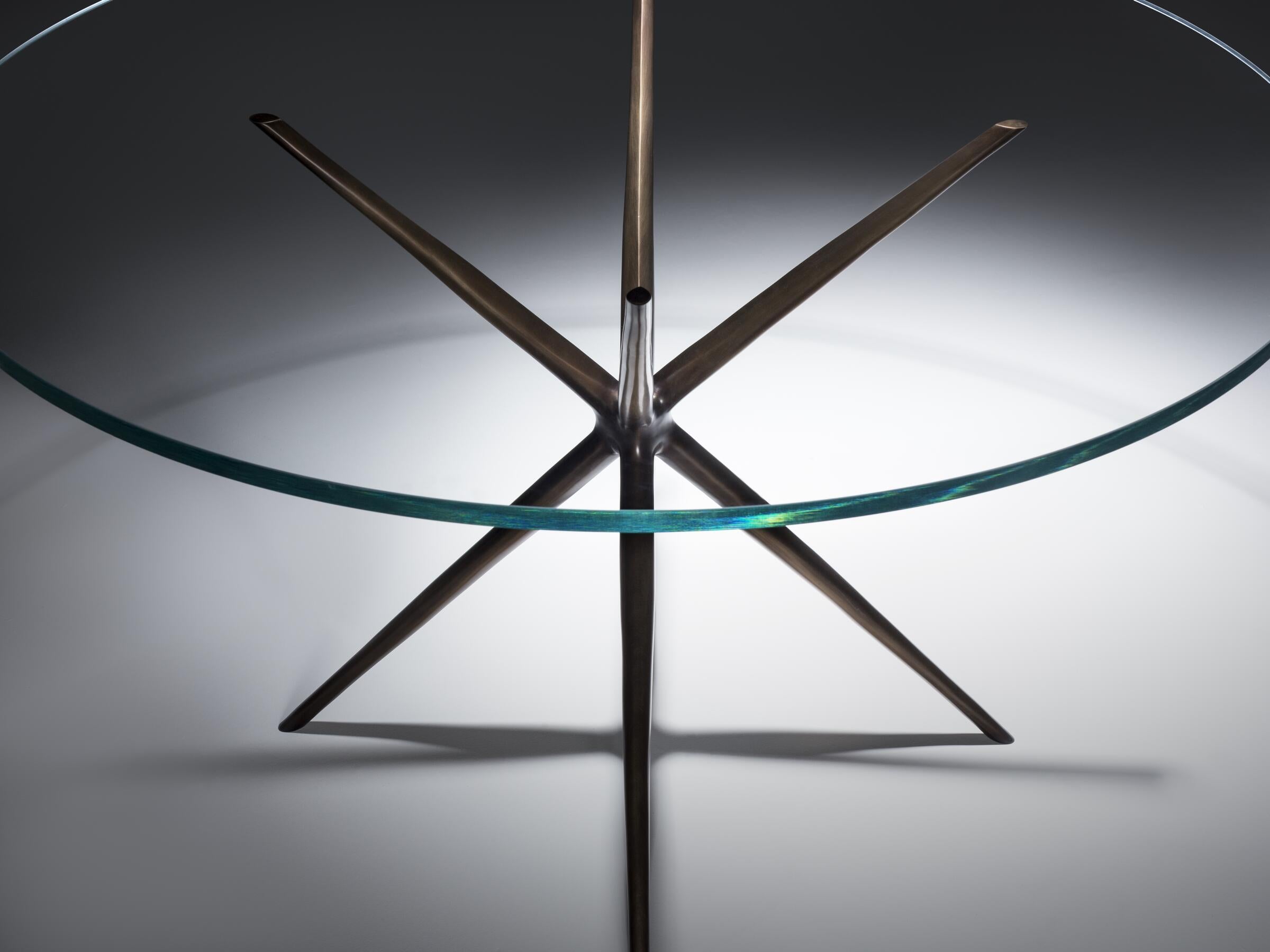 Conçue par Paul Mathieu, la table à manger Etoile est définie par sa base sculpturale en forme d'étoile. Fabriqué en bronze moulé, il présente une magnifique texture de surface qui contraste avec son plateau en verre aux lignes épurées. Dynamique