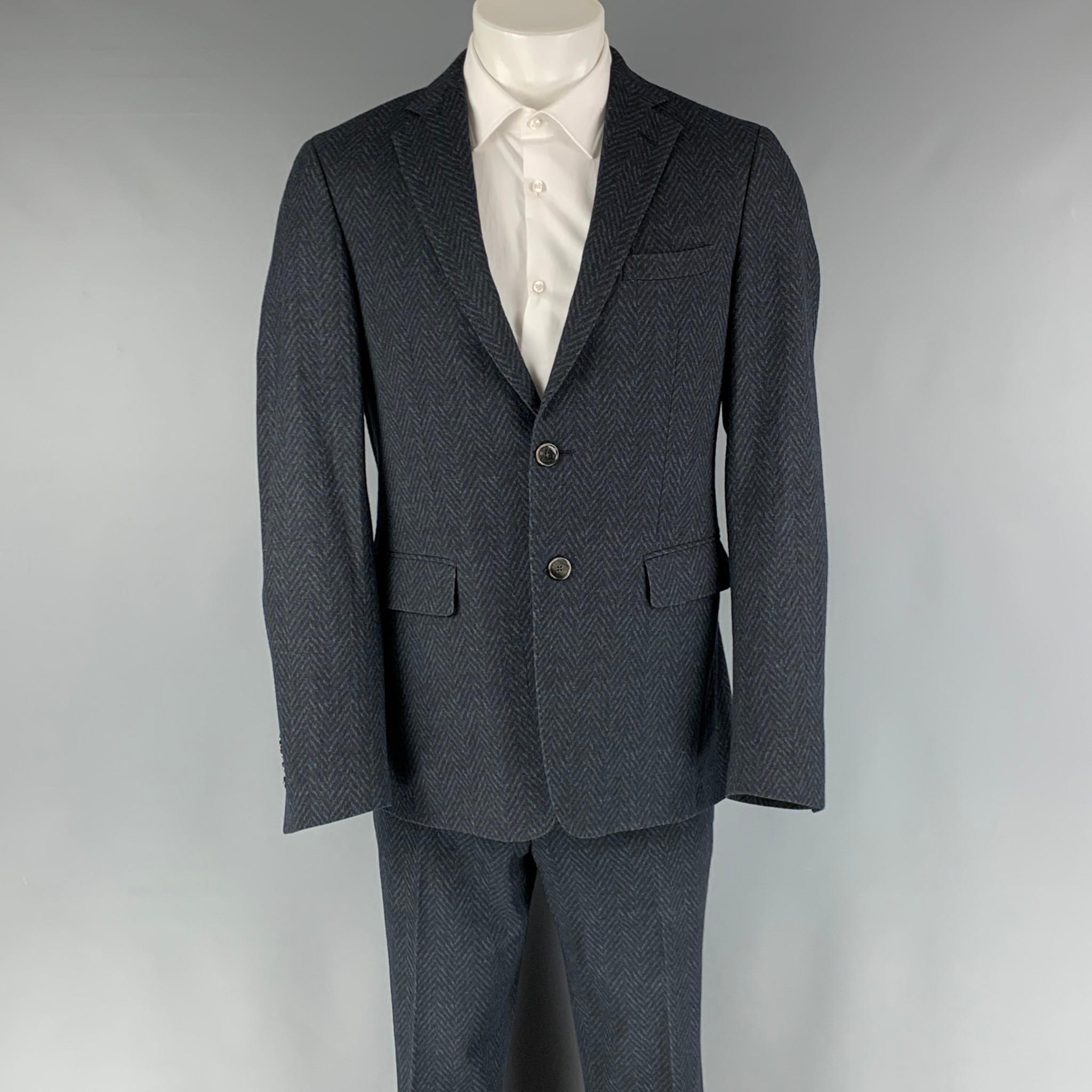 ETRO suit comes in a navy and black wool blend herringbone woven material with a full liner and includes a single breasted, two button sport coat with notch lapel and matching flat front trousers. Made in Italy.

Excellent Pre-Owned