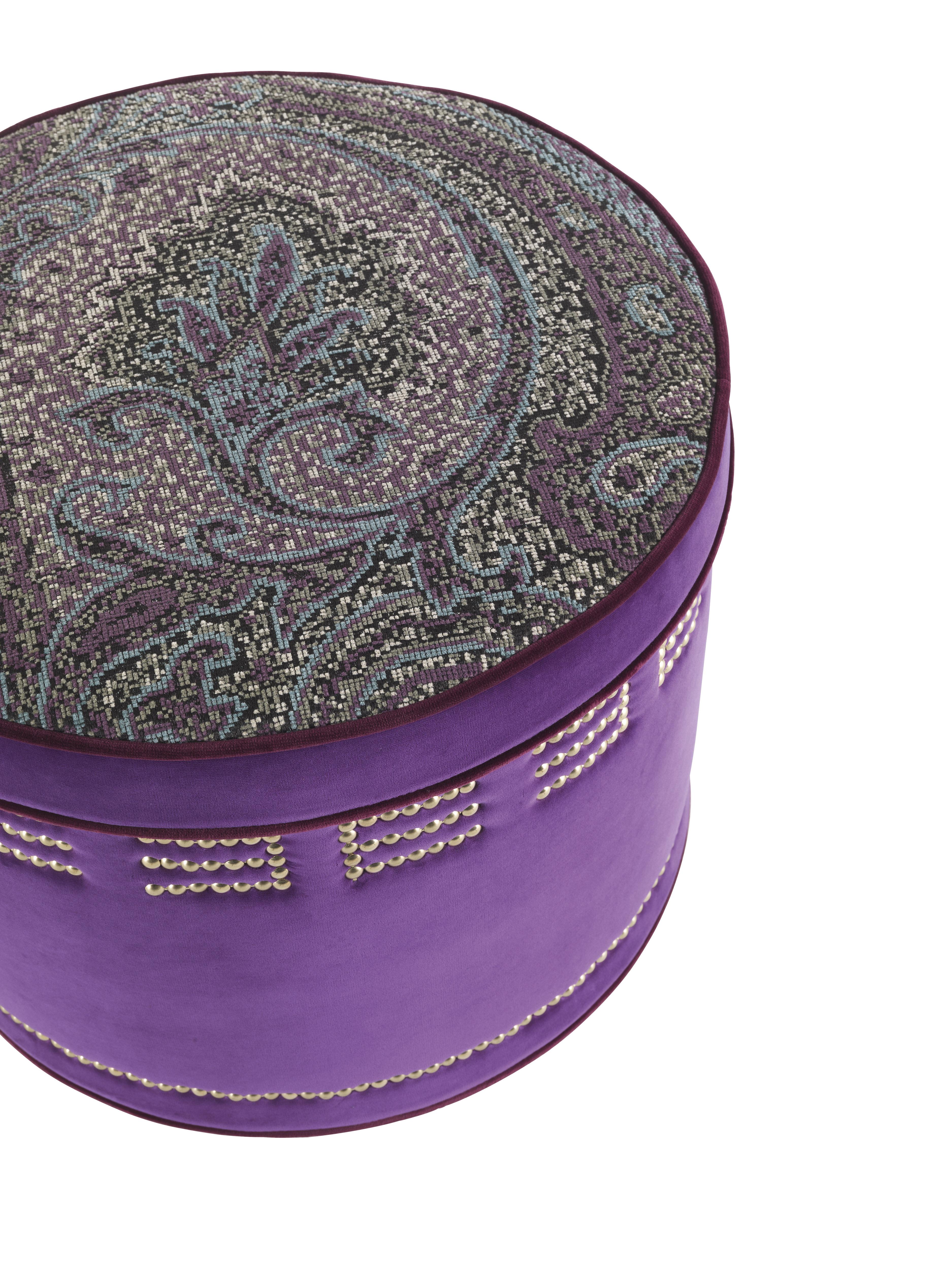 MERIAM pouf with Structure in wood and foam. Sides in velvet cat. A Venezia col. 2 Violet. Seat in fabric cat. A Rakam col. 1 Vicia. Piping in velvet cat. A Firenze col. 1 Raisin. Ornamental golden nails on the bottom. Optional decoration with Etro