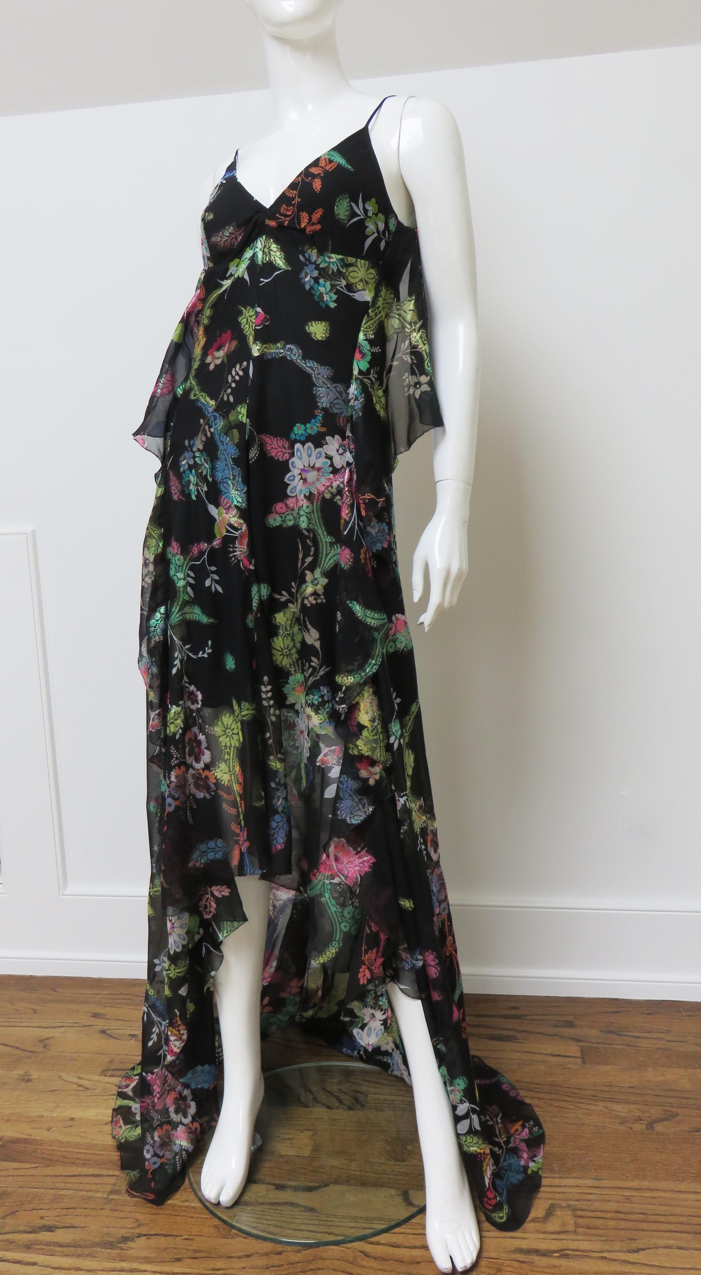 A stunning black silk maxi dress gown in a colorful elaborate flower print with iridescent accents.  It has spaghetti straps and a deep cut out back with adjustable panels of fabric draping on either side. The full skirt portion is shorter in the