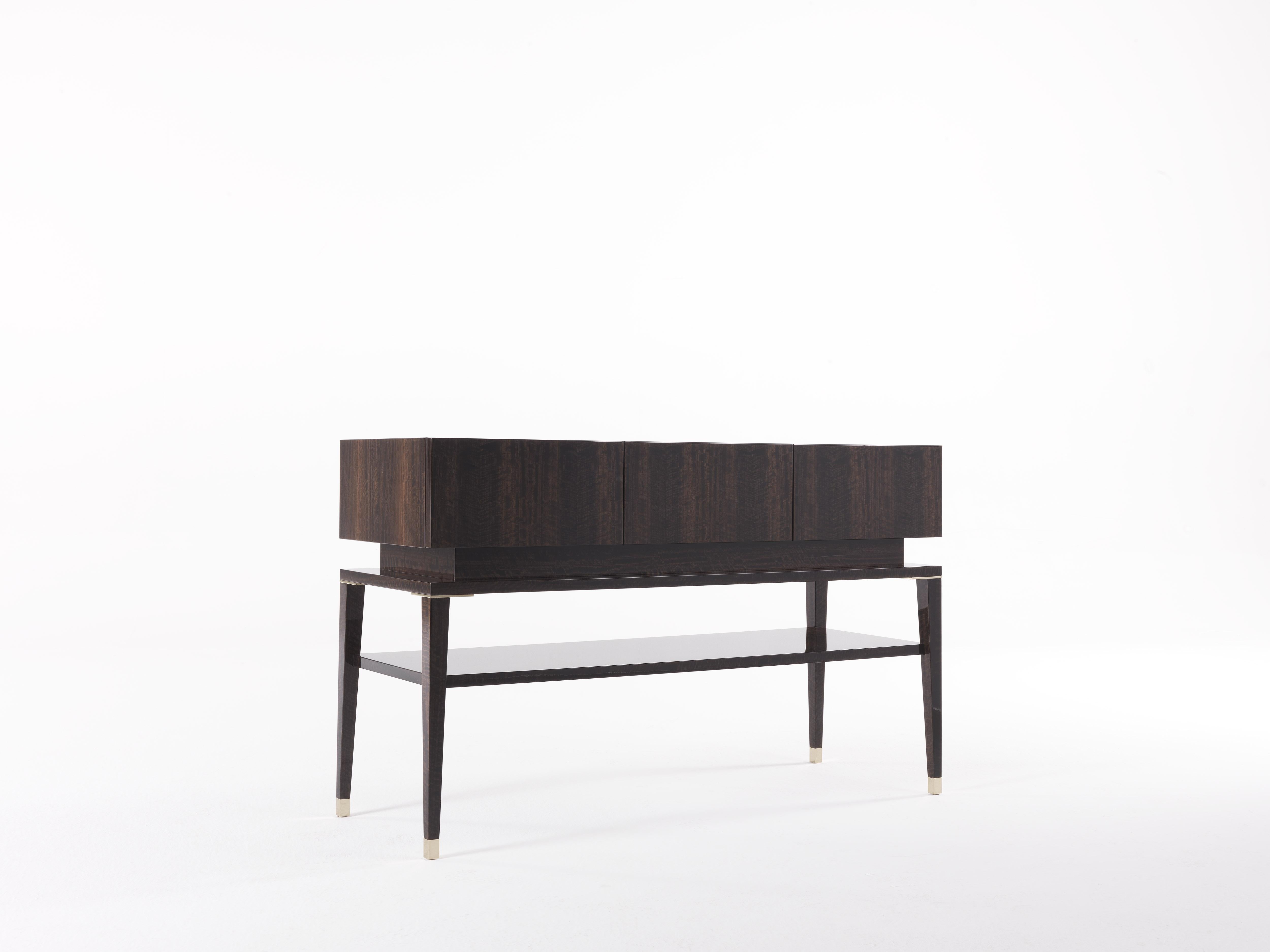 A shapely and geometric piece of furniture in which the rigorous lines of the structure in glossy smoked eucalyptus frisé wood are enhanced by the details in polished brass to create a piece of furniture that merges function and aesthetic.

Console.