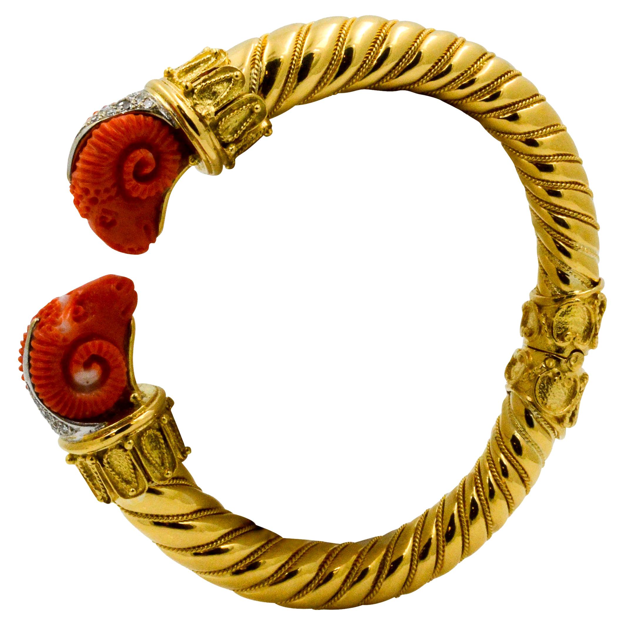 This Etruscan 18 karat yellow gold bangle has two carved coral rams accented with 20 single cut diamonds with a combined total weight of 0.40 carats. The bangle has a hinged bottom.