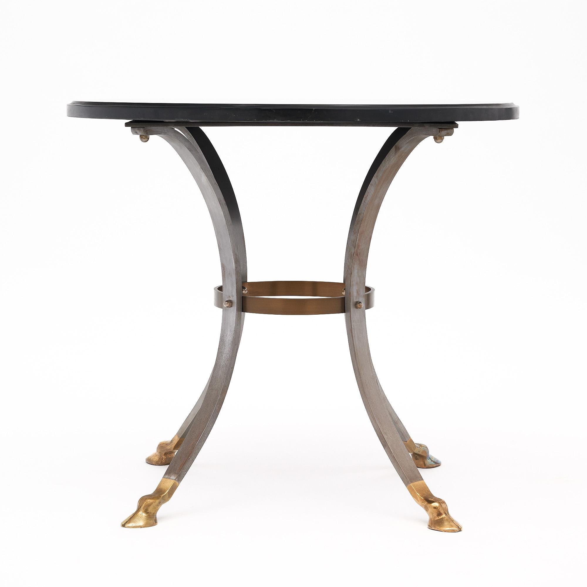 Side table from the Art Deco period in France. This table features a circular black slate top. It is supported by a base of brushed steel with a spheric brass stretcher and finely cast gilt bronze hoof feet.