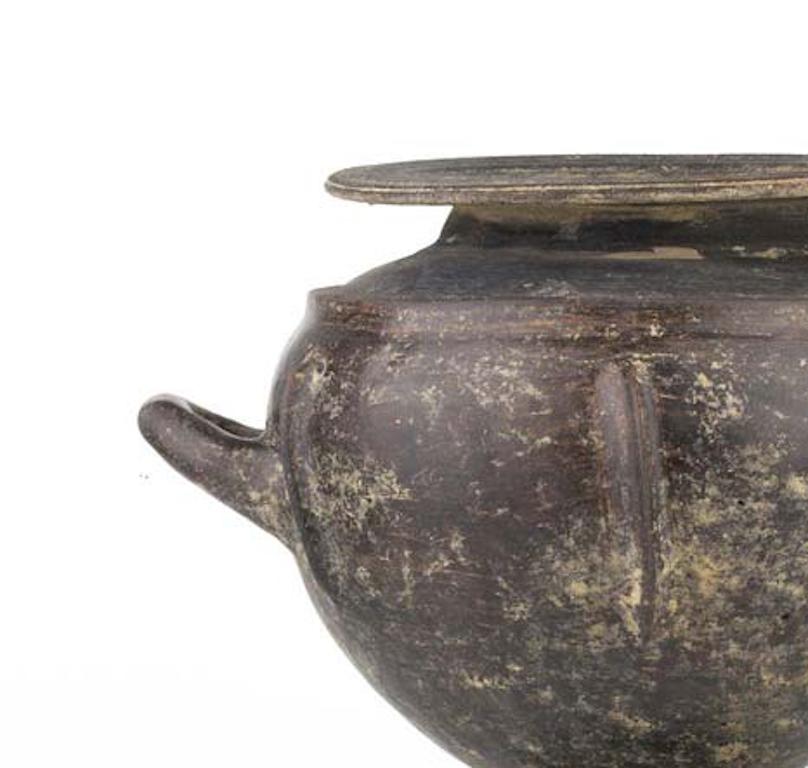 A dark brown impasto olla with globular body on high trumpet foot; on opposite sides of the body, large vertical ribs. Restored on the body and a small hole on the shoulder. 
A wonderful example of the impasto ware productions, this olla was a used