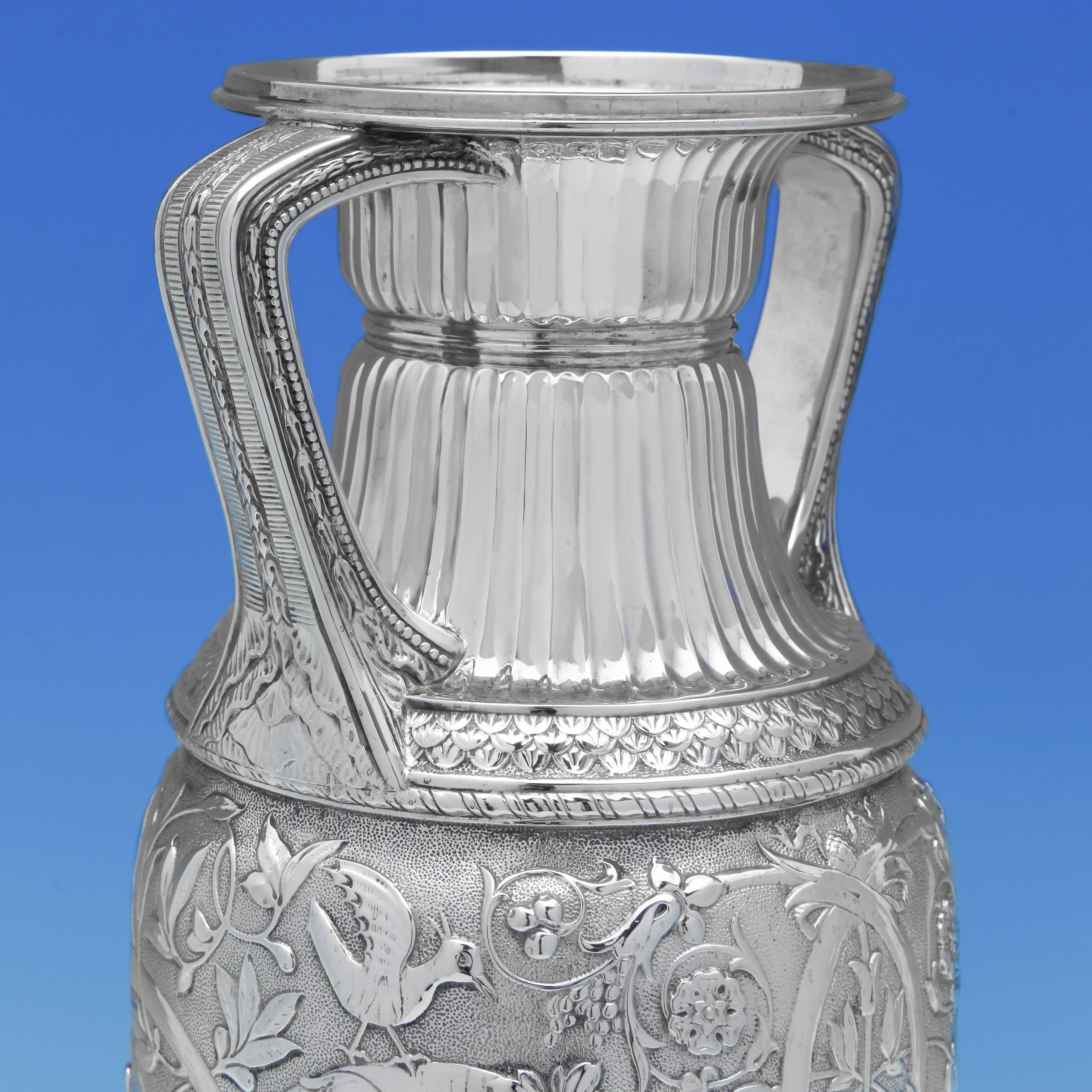Hallmarked in London in 1880, this large sterling silver vase was made by S. Smith & Son. Designed in the Etruscan Revival taste, the vase features high-relief repoussé decoration with classical figures, birds, and scrolling foliage, all finely
