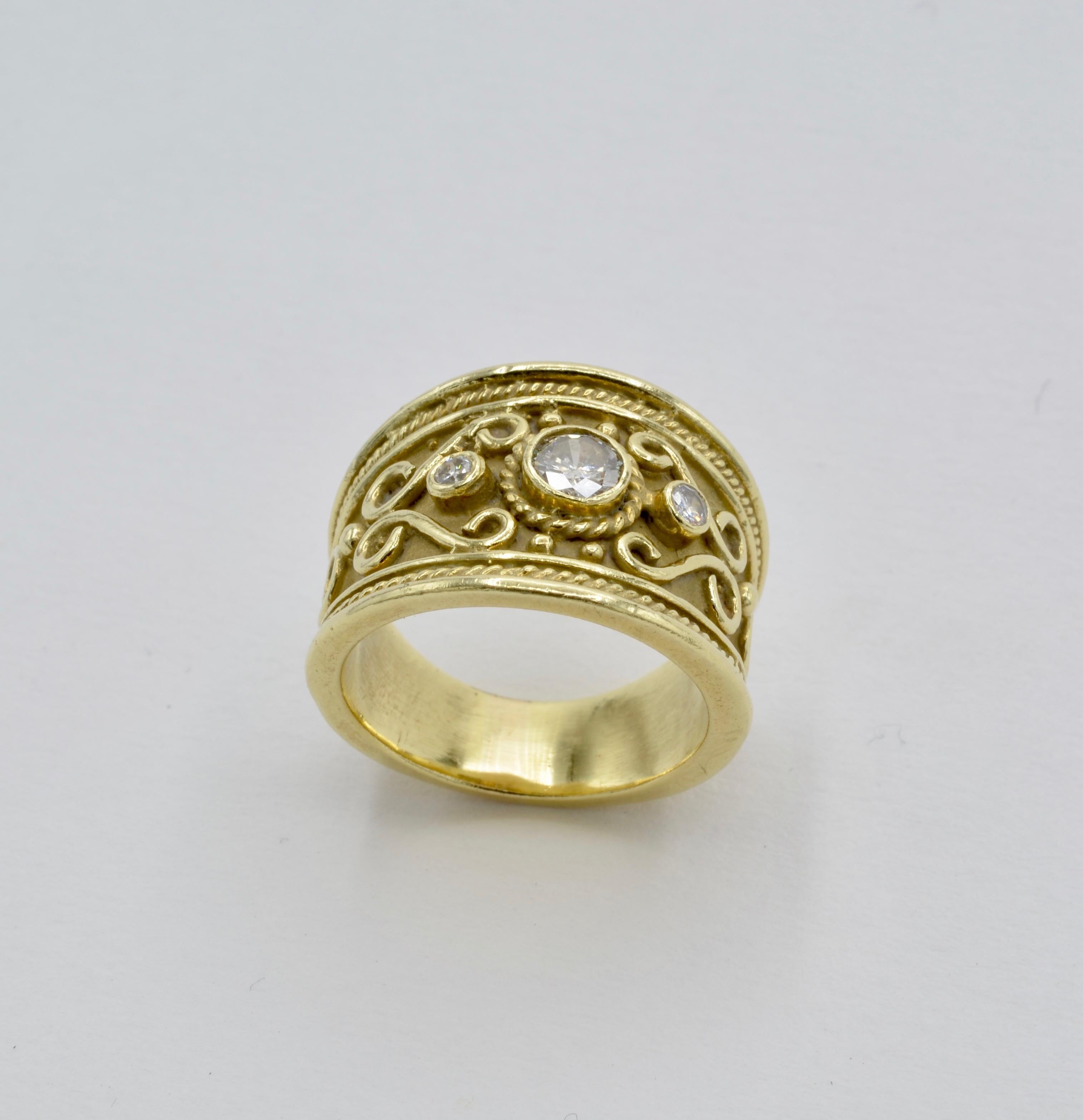 This regal wide band ring is adorned with a center diamond size 0.30 carats SI and two side accent diamonds- total diamond weight for the ring is 0.35 carats. Made of 14K Yellow gold with spirals and swirls, the Etruscan and Hellenist style ring is