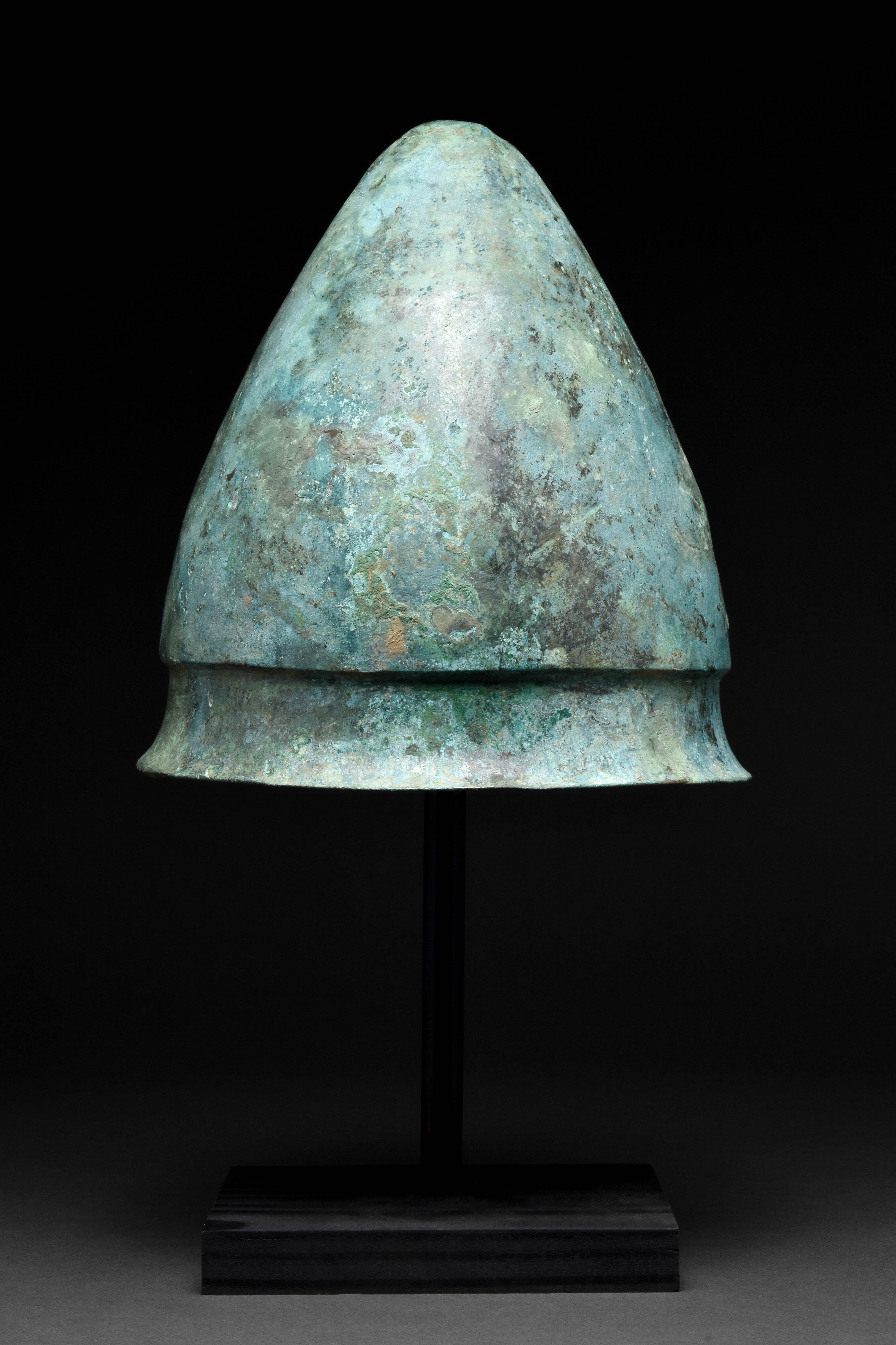 Circa 400-350 BC

A bronze Etrusco-Italic helmet, a variant of the Negau type, a regional Italian style with a characteristically conical shape. The tall, capped form resolves in a concave neck with a pronounced brim. It once would have been