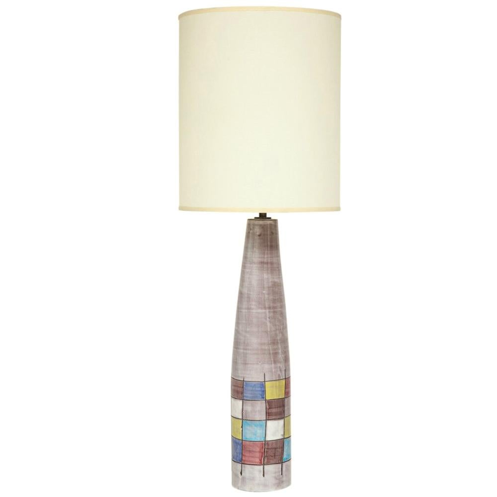 Attributed to Ettorre Sottsass for Raymor, made by Bitossi, Italy, circa 1955. Pair of tall hand thrown ceramic lamps glazed in a pinkish grey and decorated with a square patchwork pattern of yellow, blue, red, white, and sepia. This pattern was