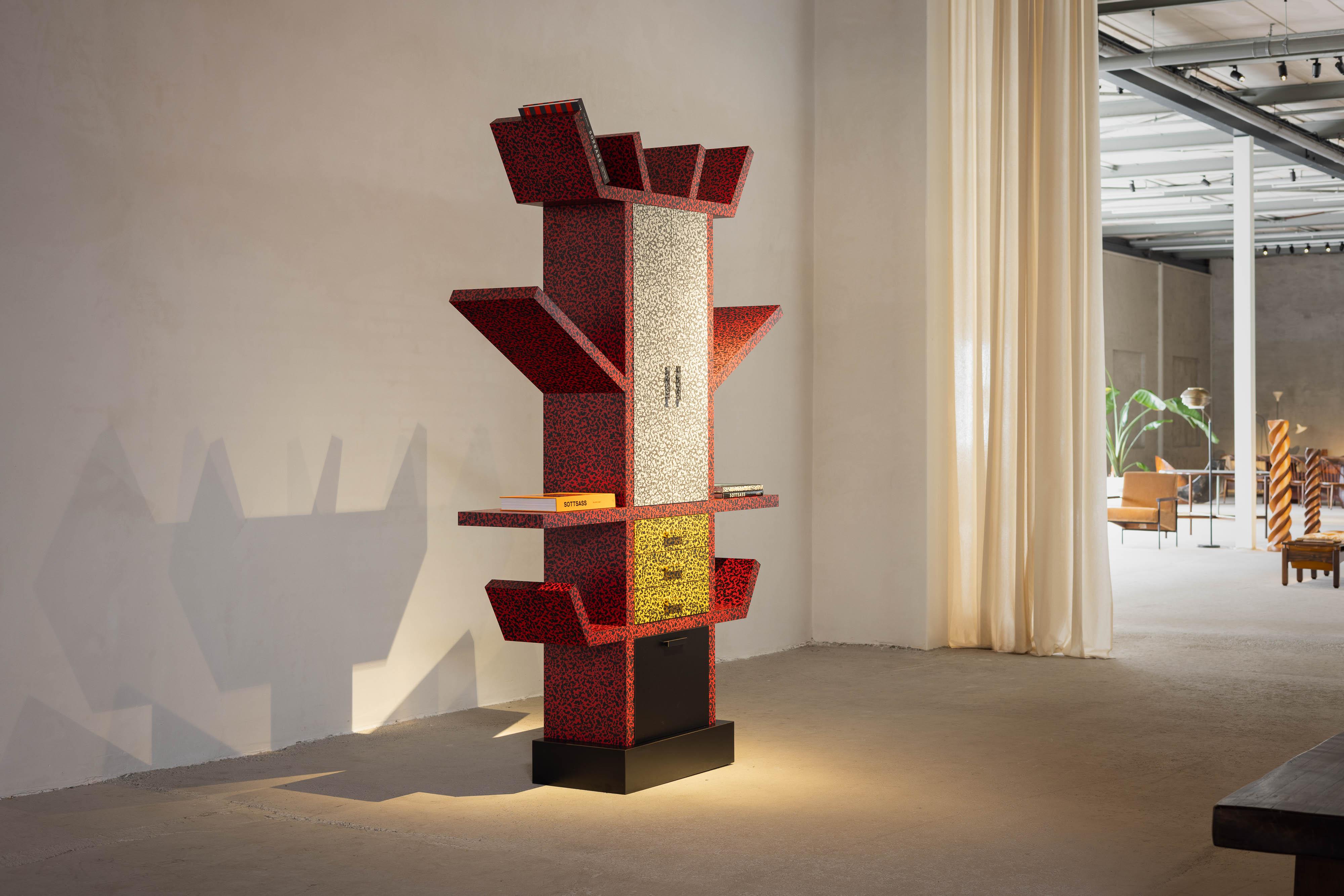 Ettore Sottsass's Casablanca cabinet boasts a totem-like profile, closely resembling his iconic Carlton room divider and Ashoka lamp. This piece stands out with its anthropomorphic silhouette, featuring vibrant red shelves that extend from a central