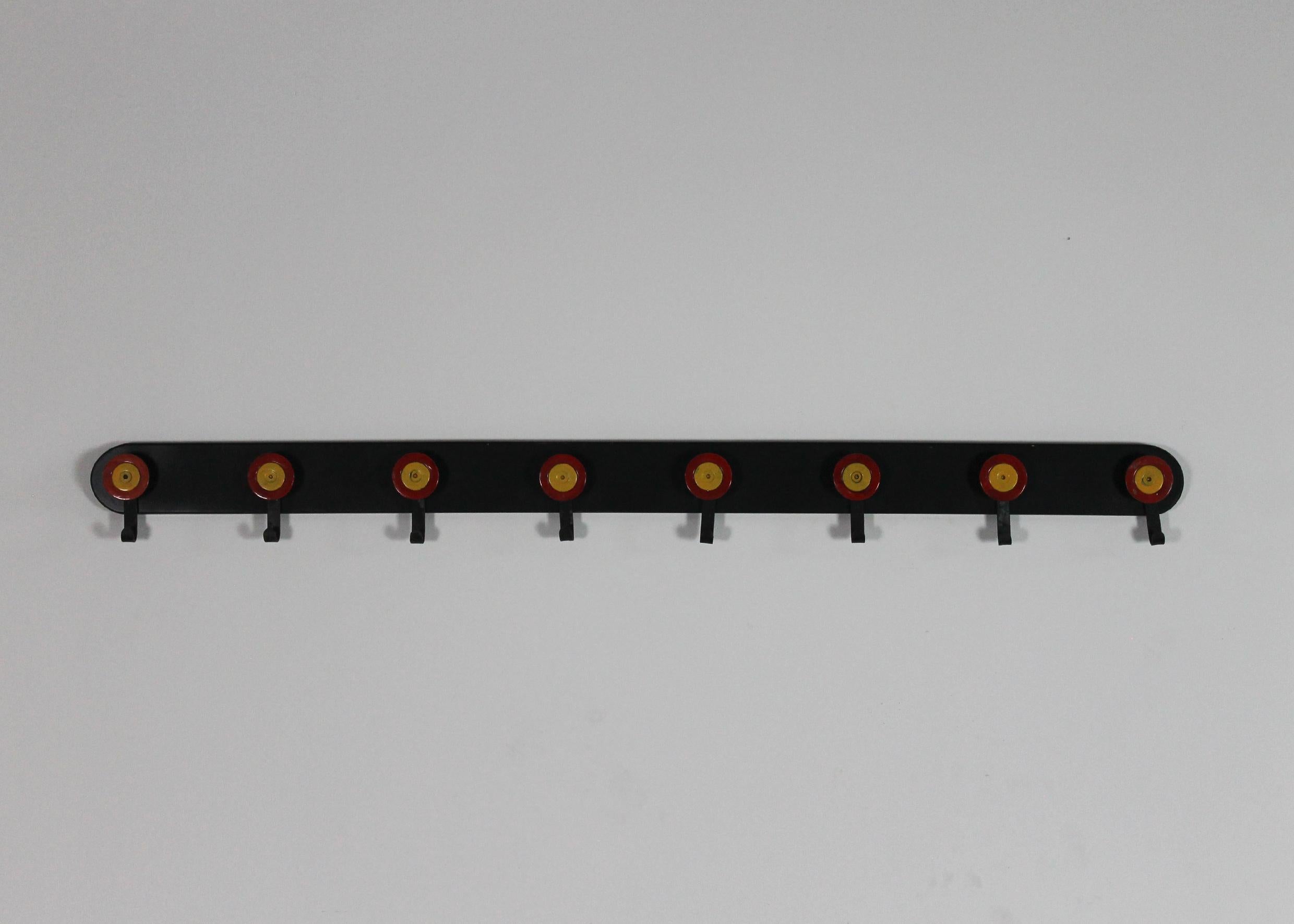 Wall coat rack or hat rack with structure in wood and eight hooks in painted metal the round shape and the color (red and yellow) chosen for the hooks remind of little archery targets. 

This coat rack was designed by Ettore Sottsass and
