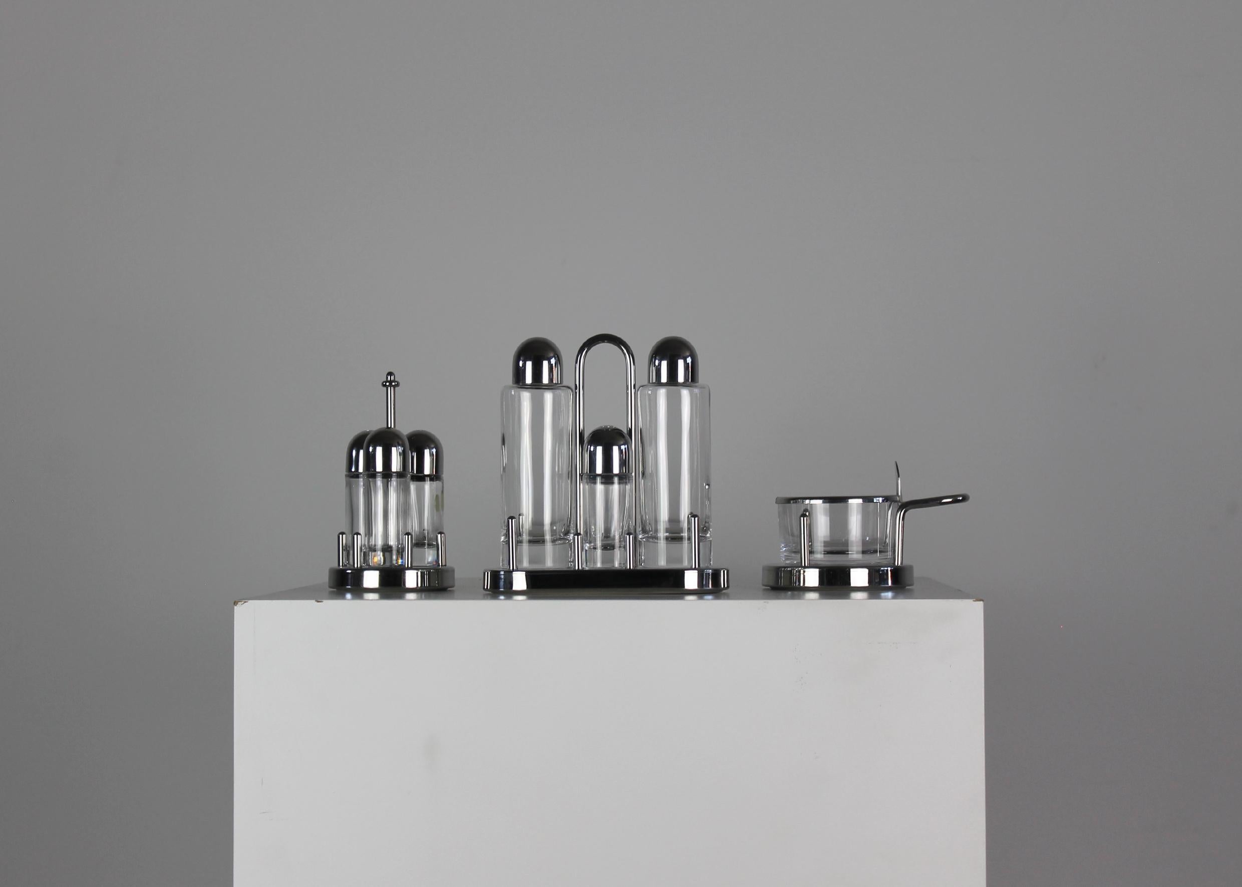 Cruet set composed of one complete set with an oil jug, vinegar jug, salt and pepper shaker, one set with three spices shakers, and a cheese pot, each piece was realized in glass and stainless steel.
This cruet set was designed by Ettore Sottsass in