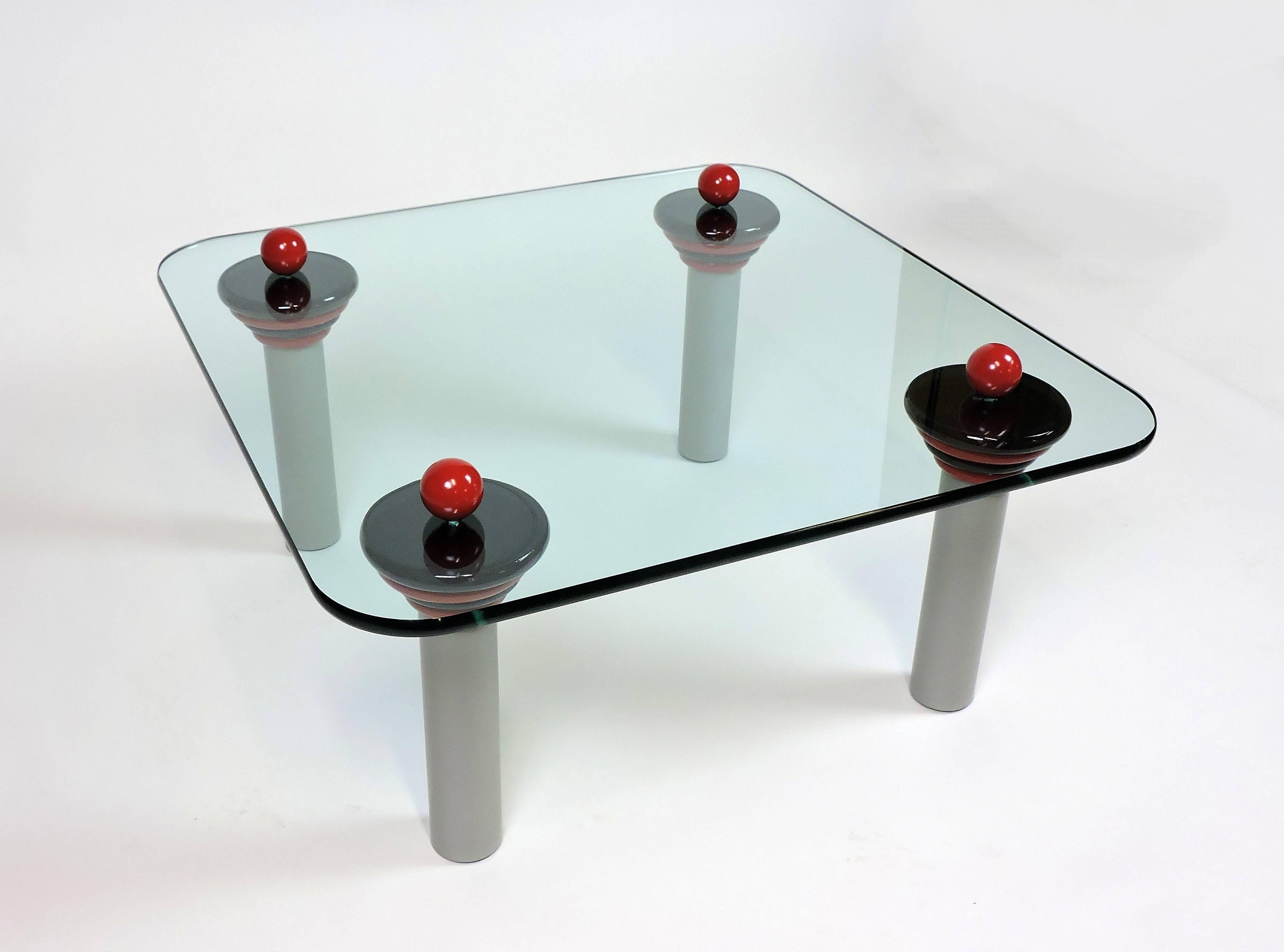 Fun and colorful coffee table in the style of Ettore Sottsass. This high quality table has wooden red balls and black and red circular discs that rest on top of gray metal tubular legs. It has a 3/4 inch thick glass top with a polished edge.