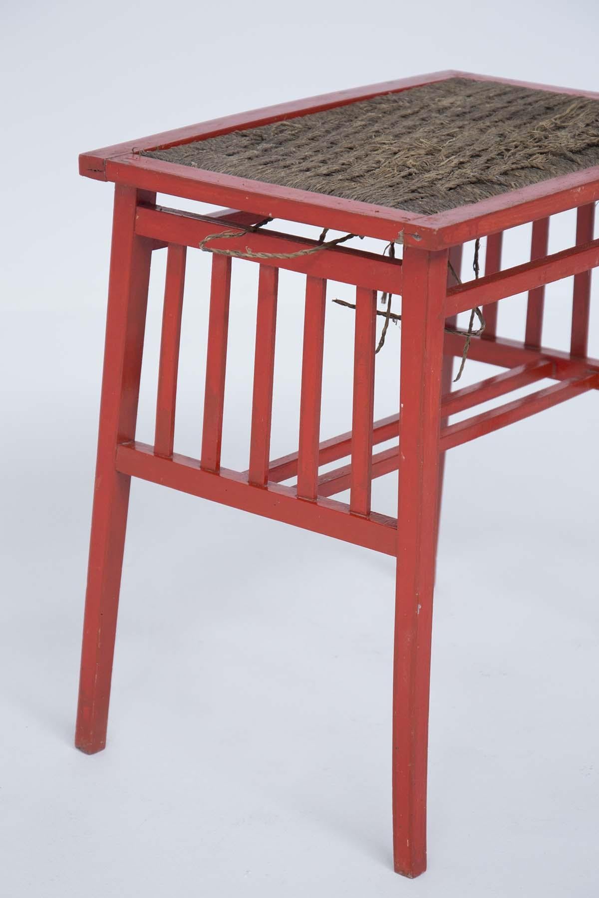 Wooden coffee table painted in the style of Ettore Sottsass designed in the 1950s. 
The frame is made of red painted wood and has four legs. The top is made of woven rope. The seat is embroidered with a row of five wooden rods. The wooden coffee