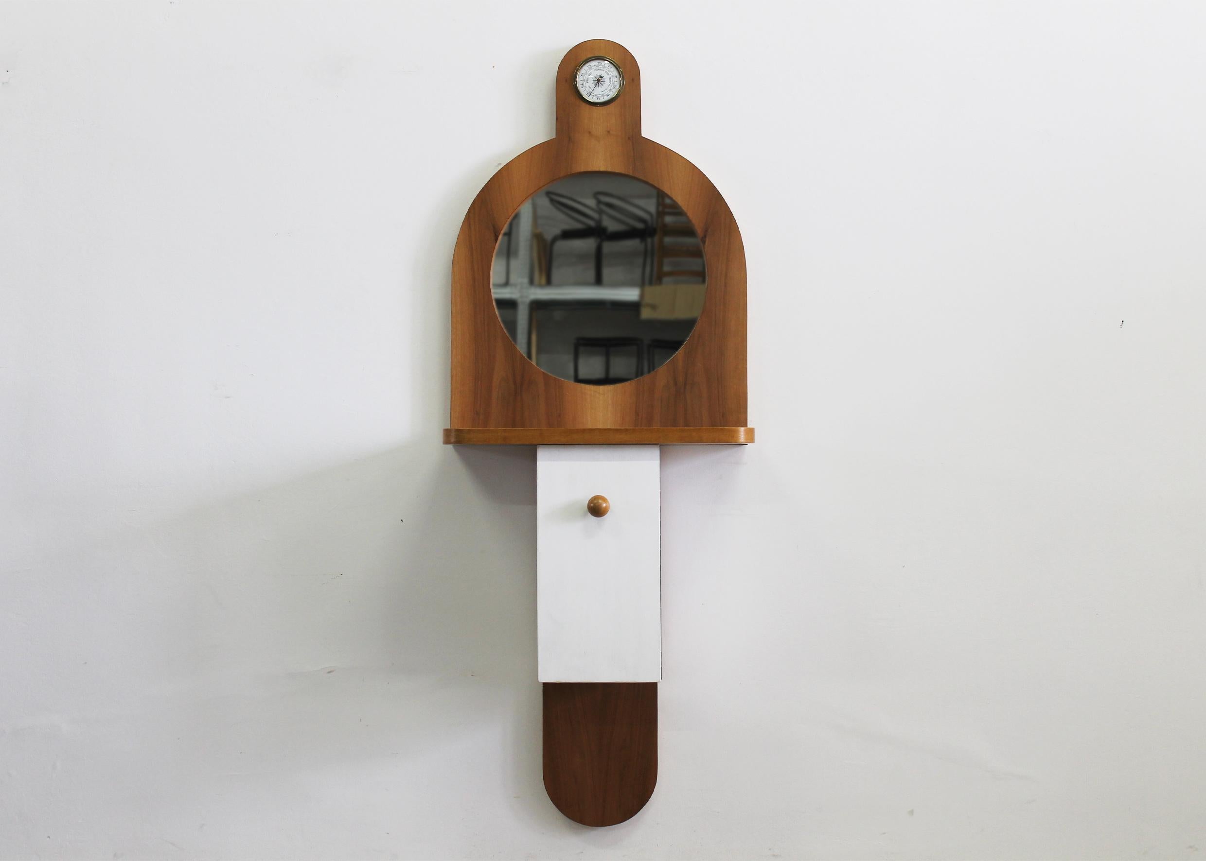 Tempus wall cabinet in wood and white lacquered wood, with a frontal door panel a mirror, and a barometer, designed by Ettore Sottsass and produced by Poltronova in the 1960s. 

