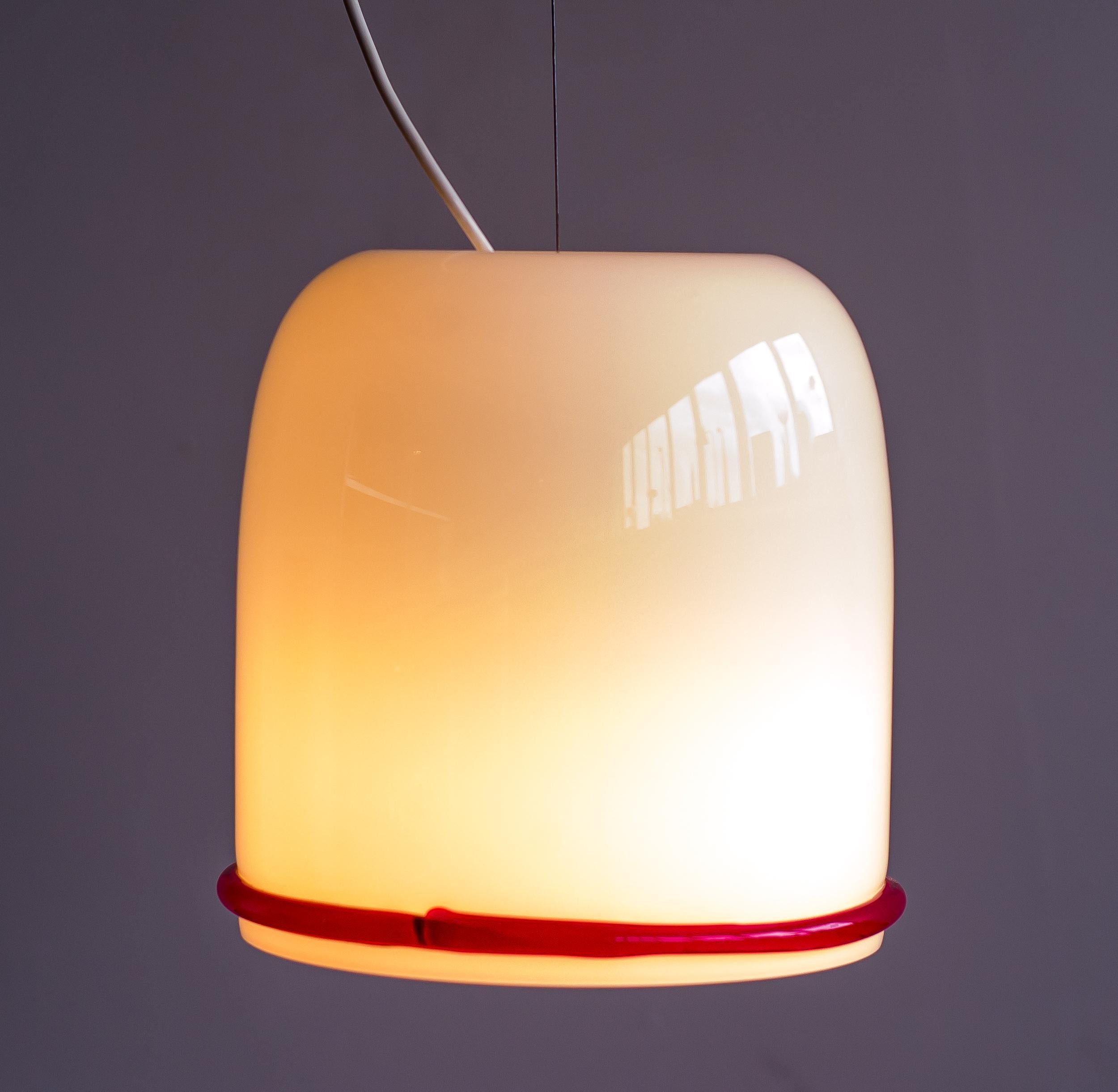 Clear glass over white glass pendant with clear red glass ribbon, designed by Ettore Sottsass for Vistosi. 
Height adjustable steel cable. The original white enameled steel canopy is included.
Signed Vistosi.

Ettore Sottsass was an Italian
