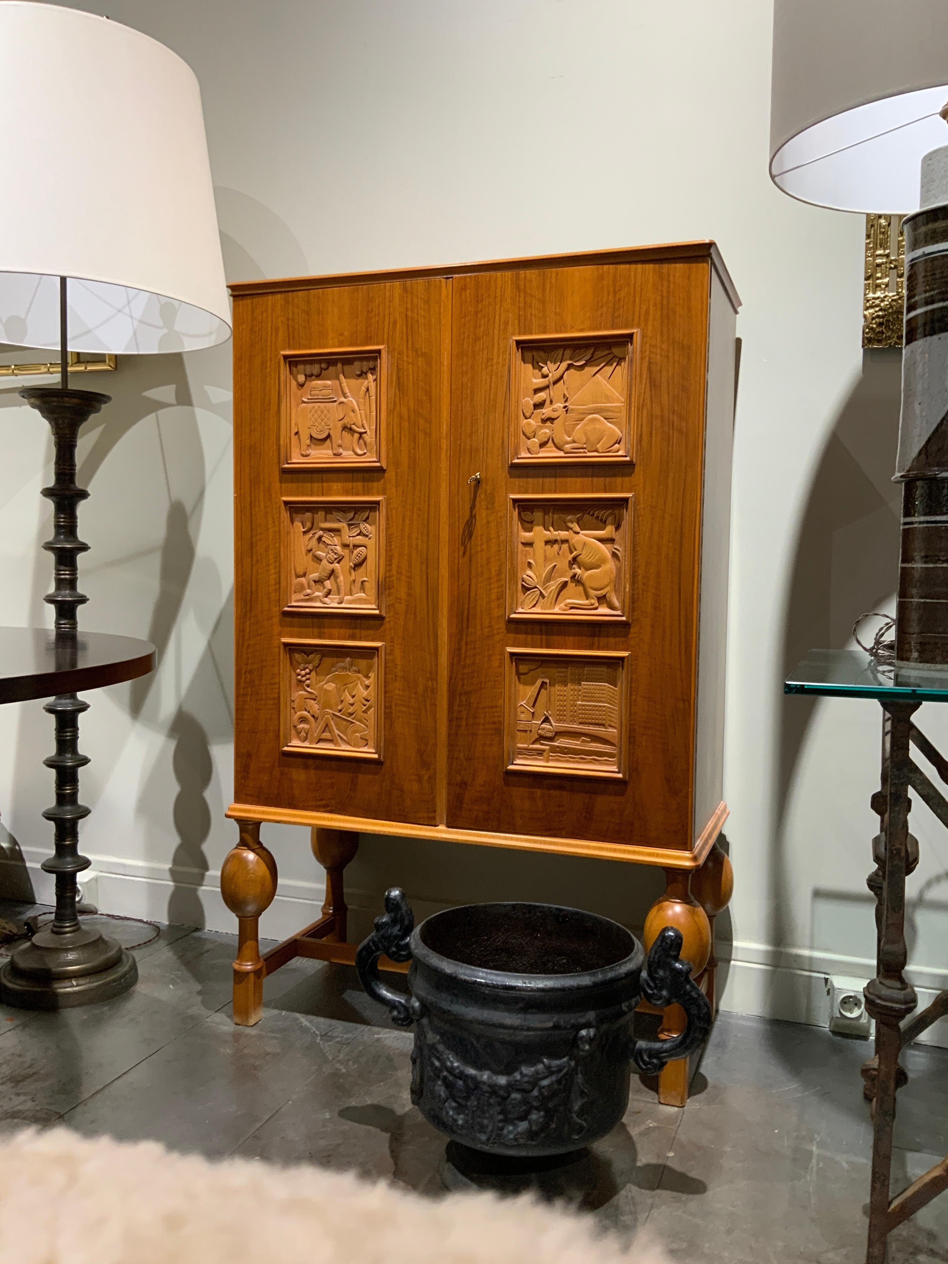 Très élégante armoire en noyer attribuée à Elegen HOLGUND Suède vers 1950
Paire de portes à décor sculpté représentant 6 continents 
Clé incluse 
