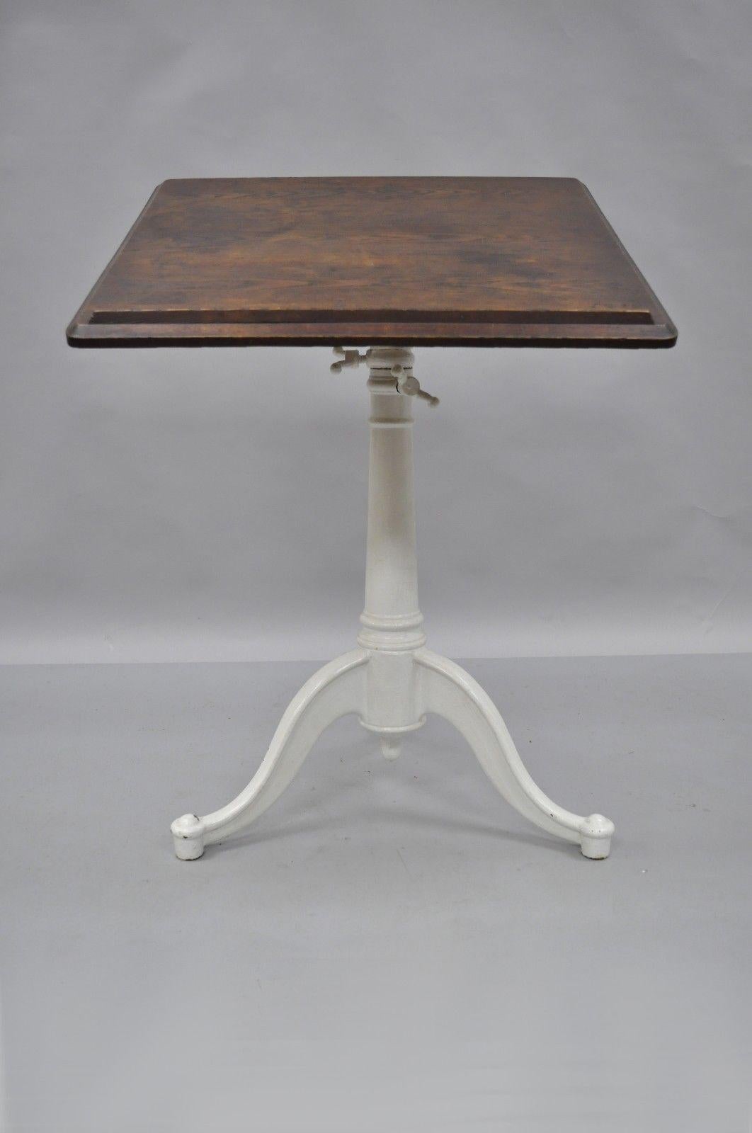 Antique cast iron and wood small drafting work table by Eugene Dietzgen. Item features cast iron tripod base, solid wood top, original tag, adjustable height and tilt, quality American craftsmanship. Later added white painted finish to base, circa