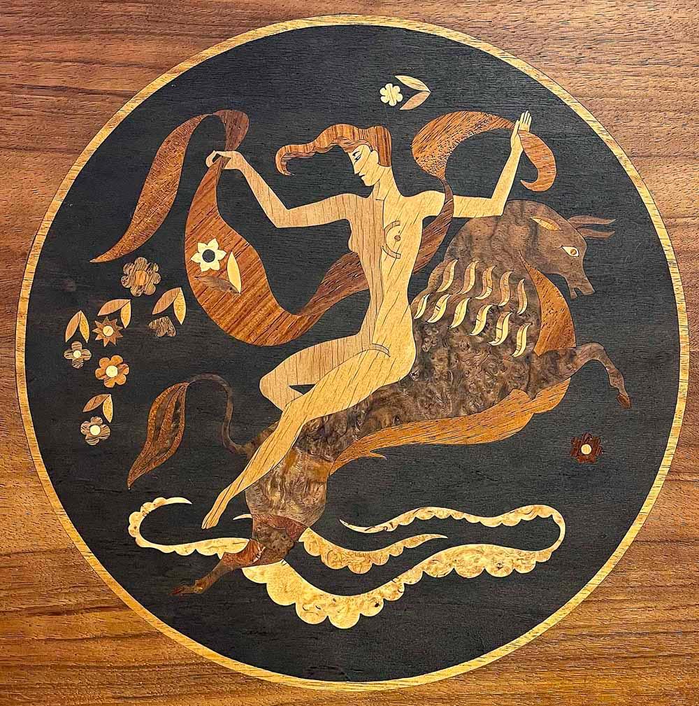 This masterwork of inlaid wood -- in stunning, interlocking pieces of burled walnut and maple, mahogany and beech -- depicts Europa riding the bull, a classic story from Greek mythology.  The artist was Andrew Szoeke, who was America's greatest